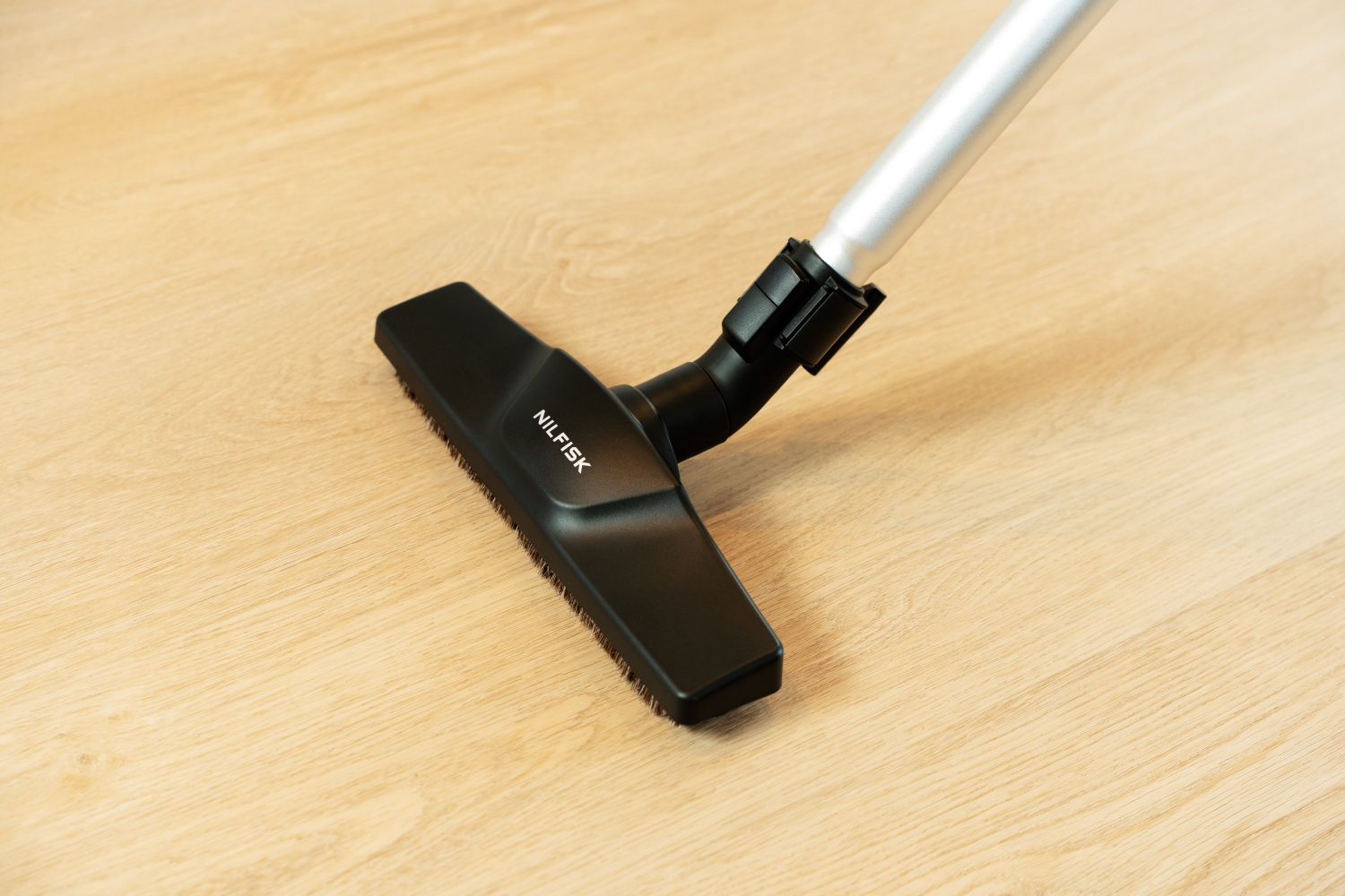 Cabezal de aspiradora negro con logo NILSFISK sobre suelo de madera clara.