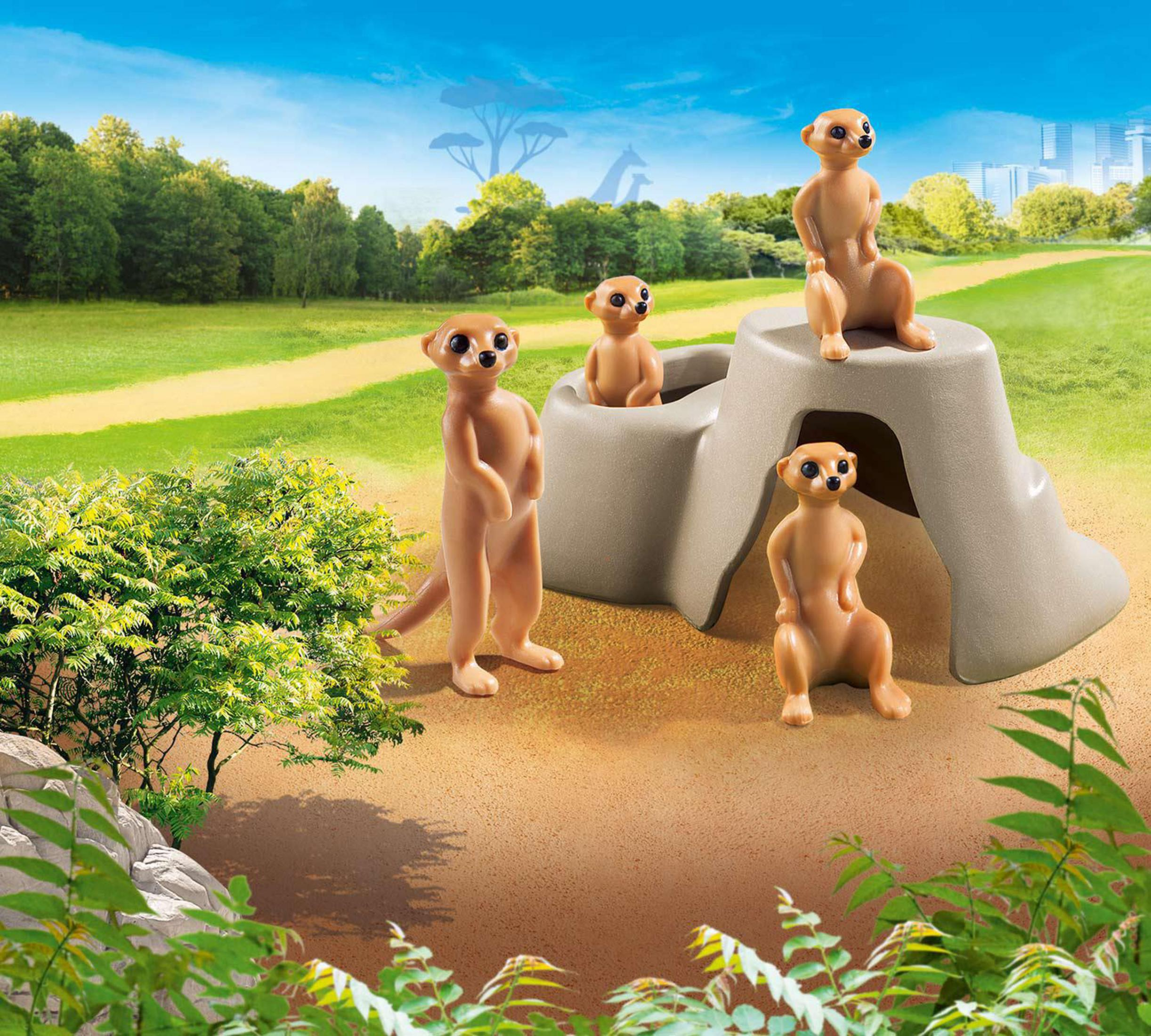 Quatre suricates se tiennent debout et assis près d'un rocher dans un paysage de savane.