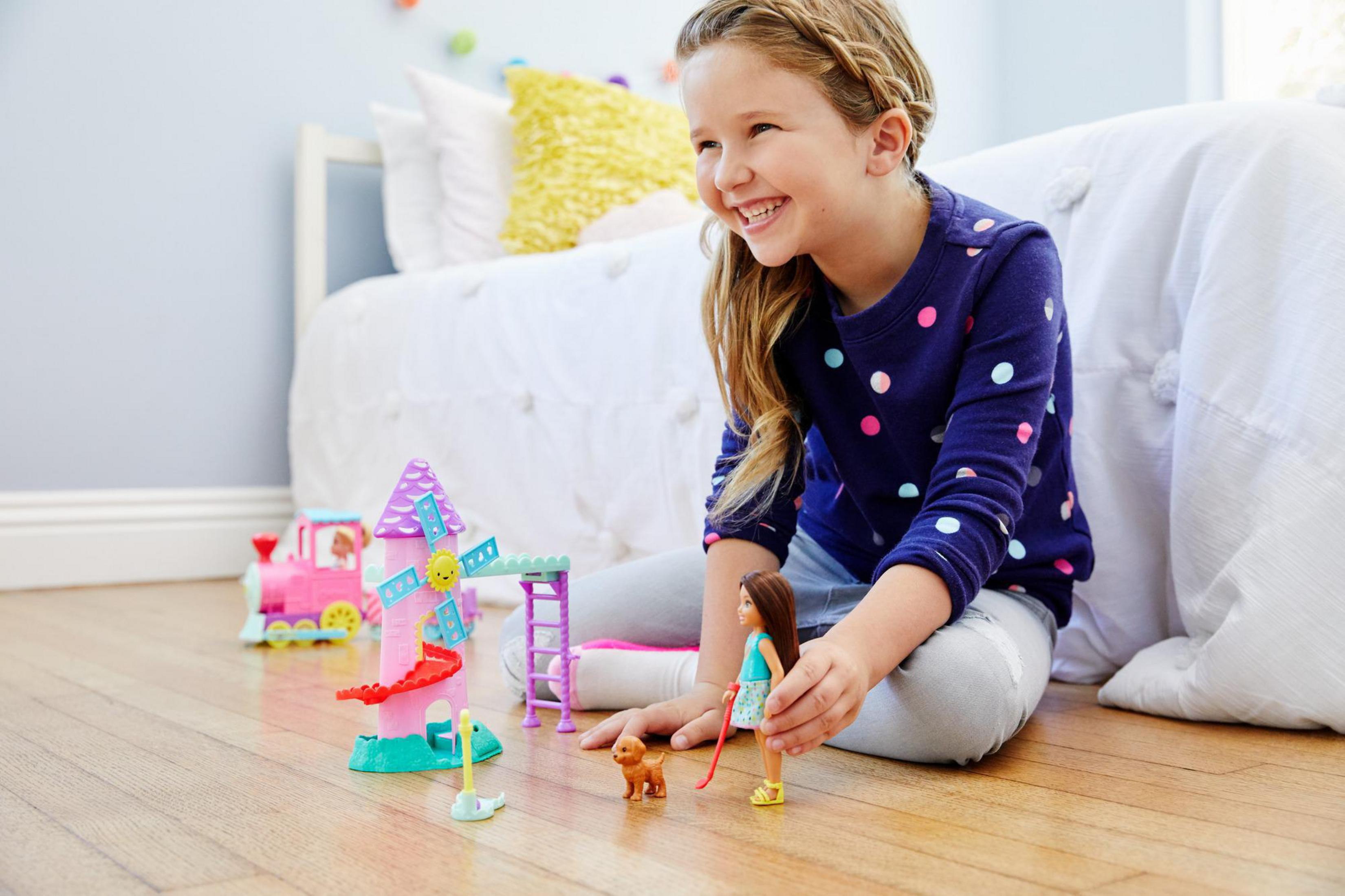 Ein Mädchen spielt mit Spielzeug auf dem Boden. Ein rosa Zug und eine Windmühle.