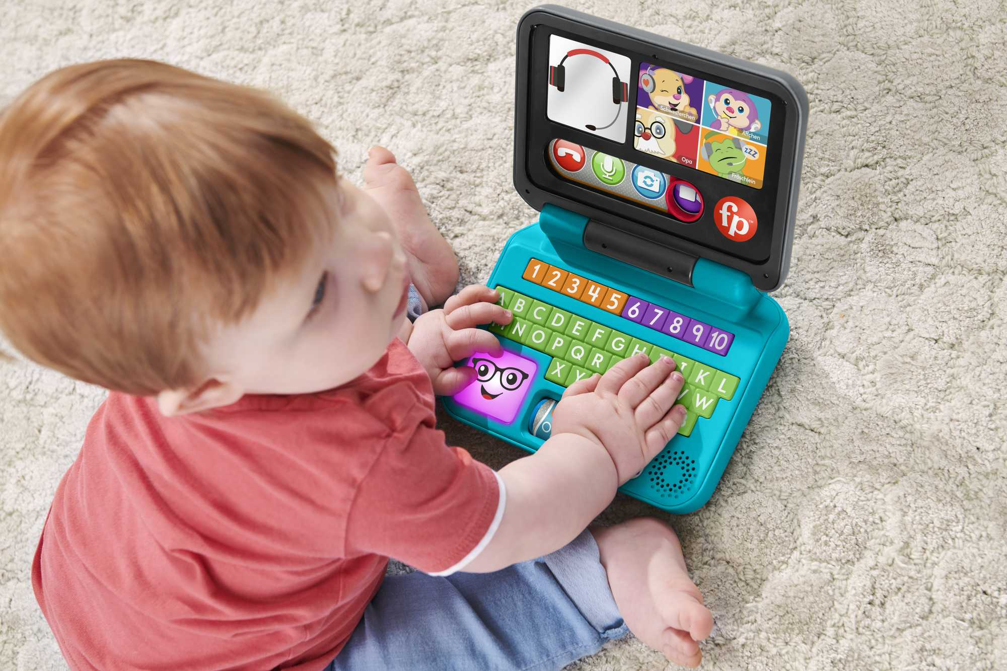 Ein Baby spielt mit einem bunten Spielzeug-Laptop auf einem Teppich.