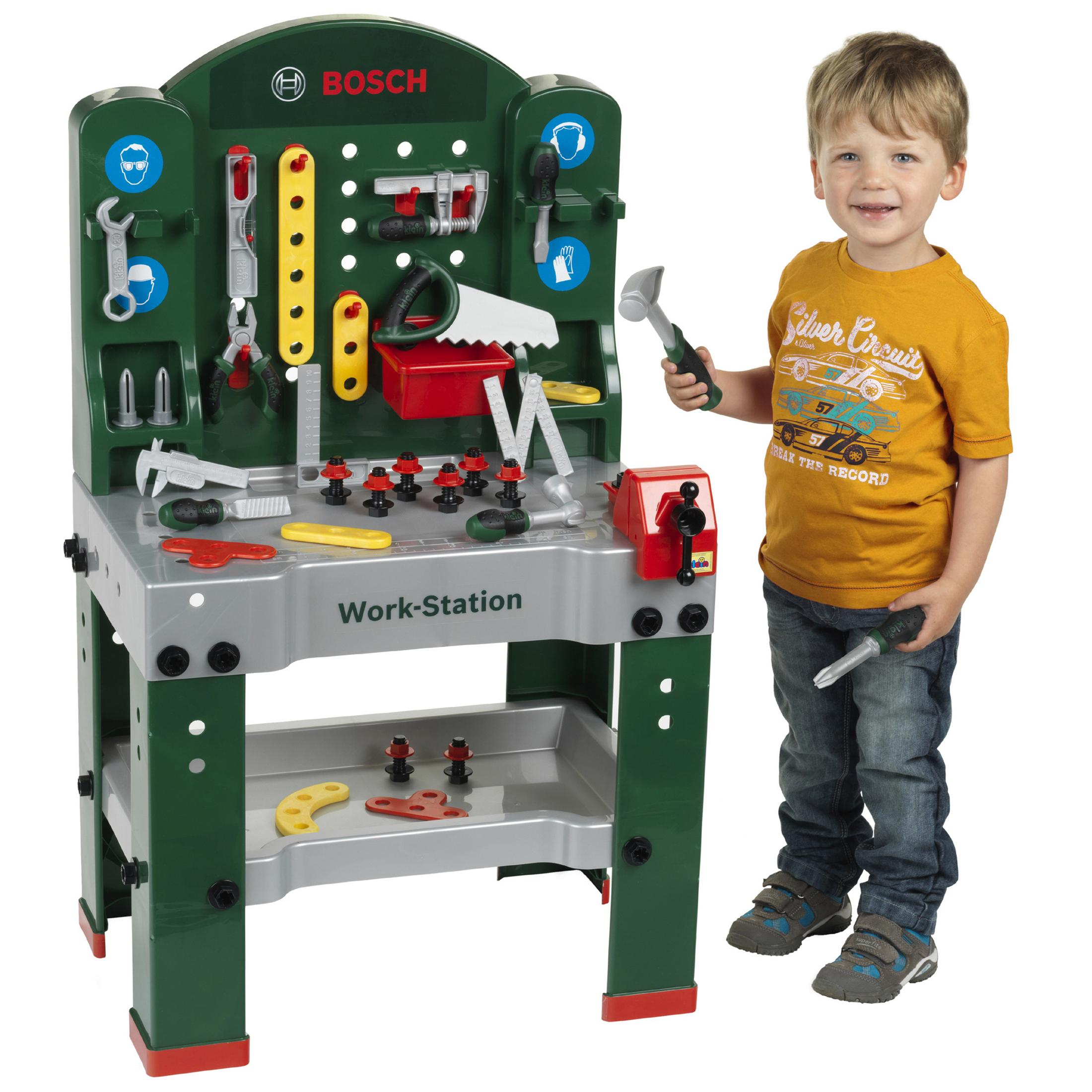 Un bambino accanto a un banco da lavoro Bosch verde con attrezzi, tiene un martello.