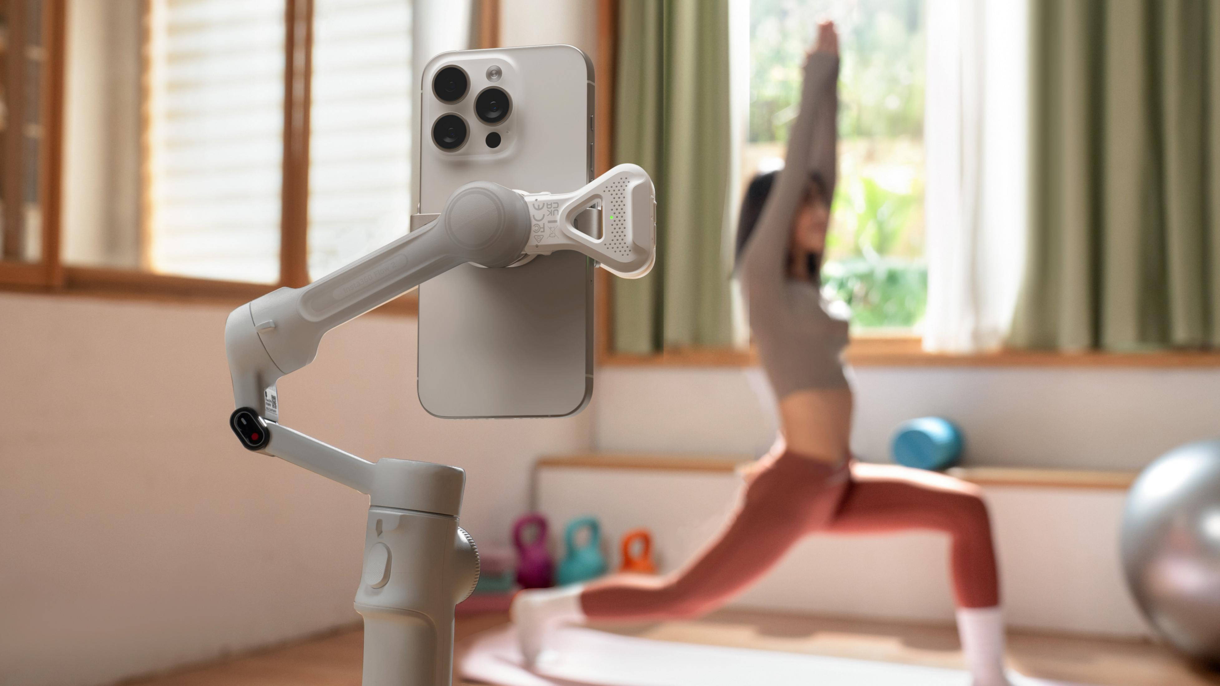 Ein Smartphone auf einem Gimbal filmt eine Frau beim Yoga vor einem Fenster.