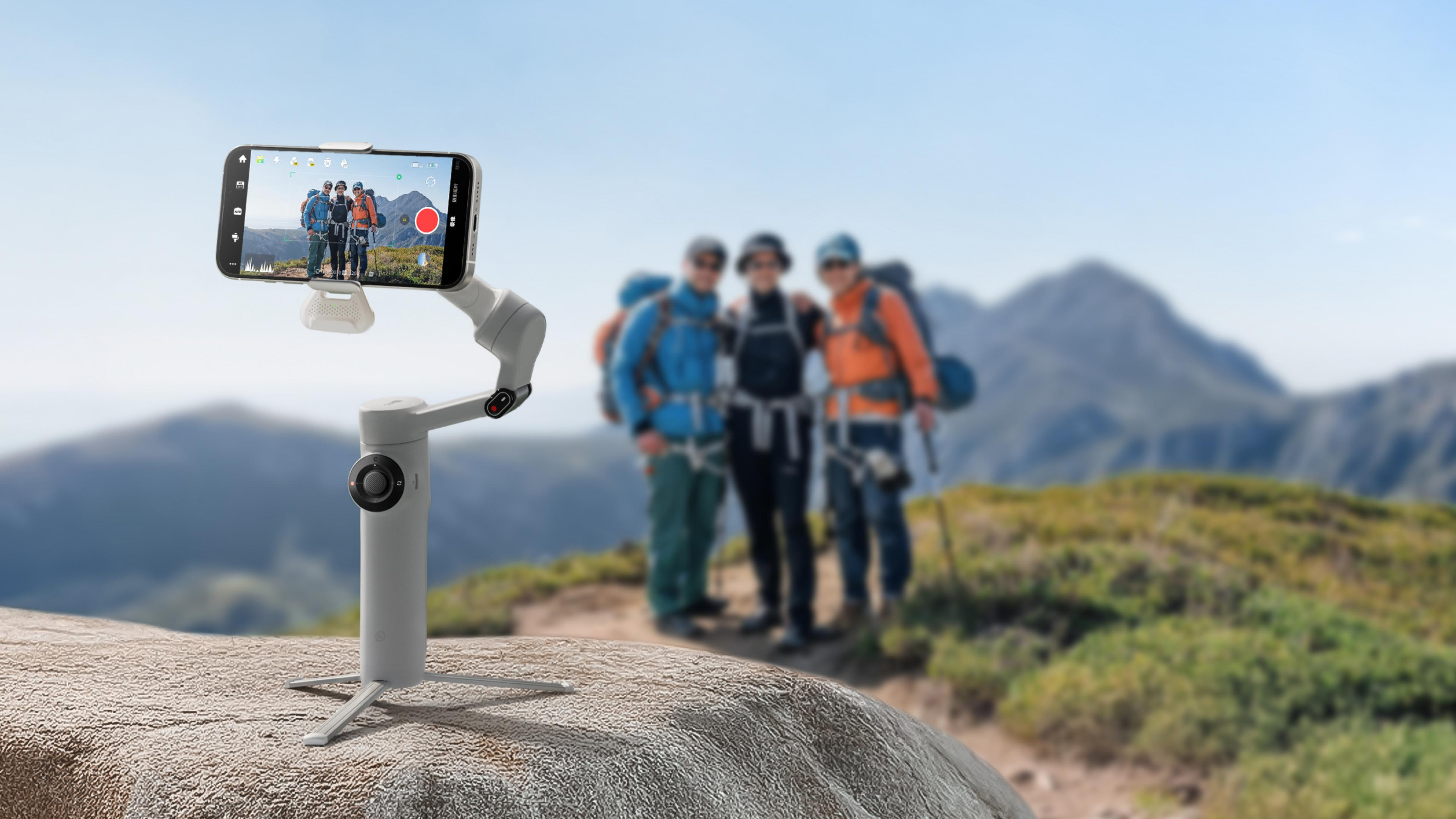 Ein Gimbal mit Smartphone filmt drei Wanderer in den Bergen. Ein Felsblock im Vordergrund.
