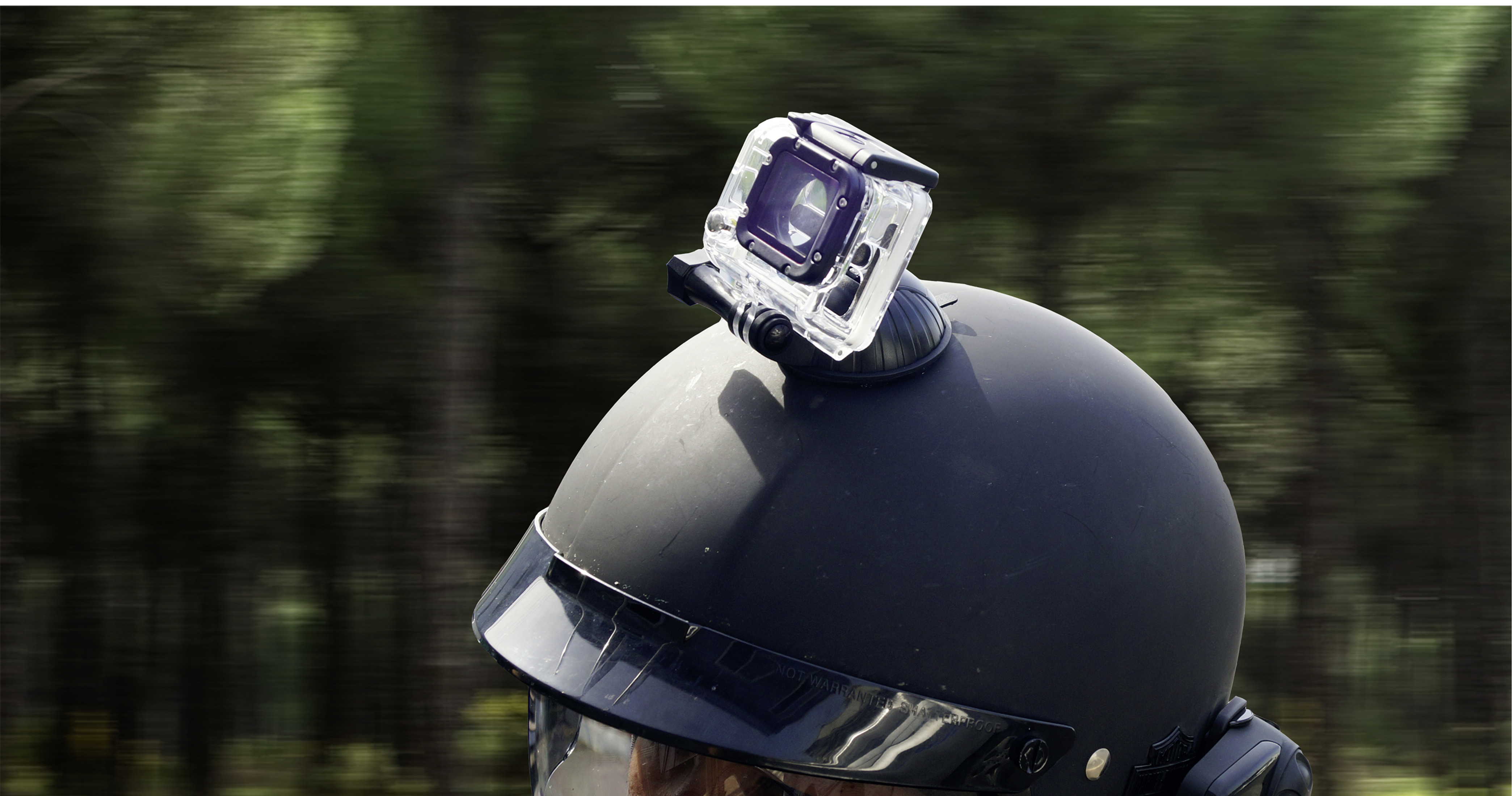 Ein schwarzer Helm mit einer Action-Kamera, mit Bäumen im Hintergrund.