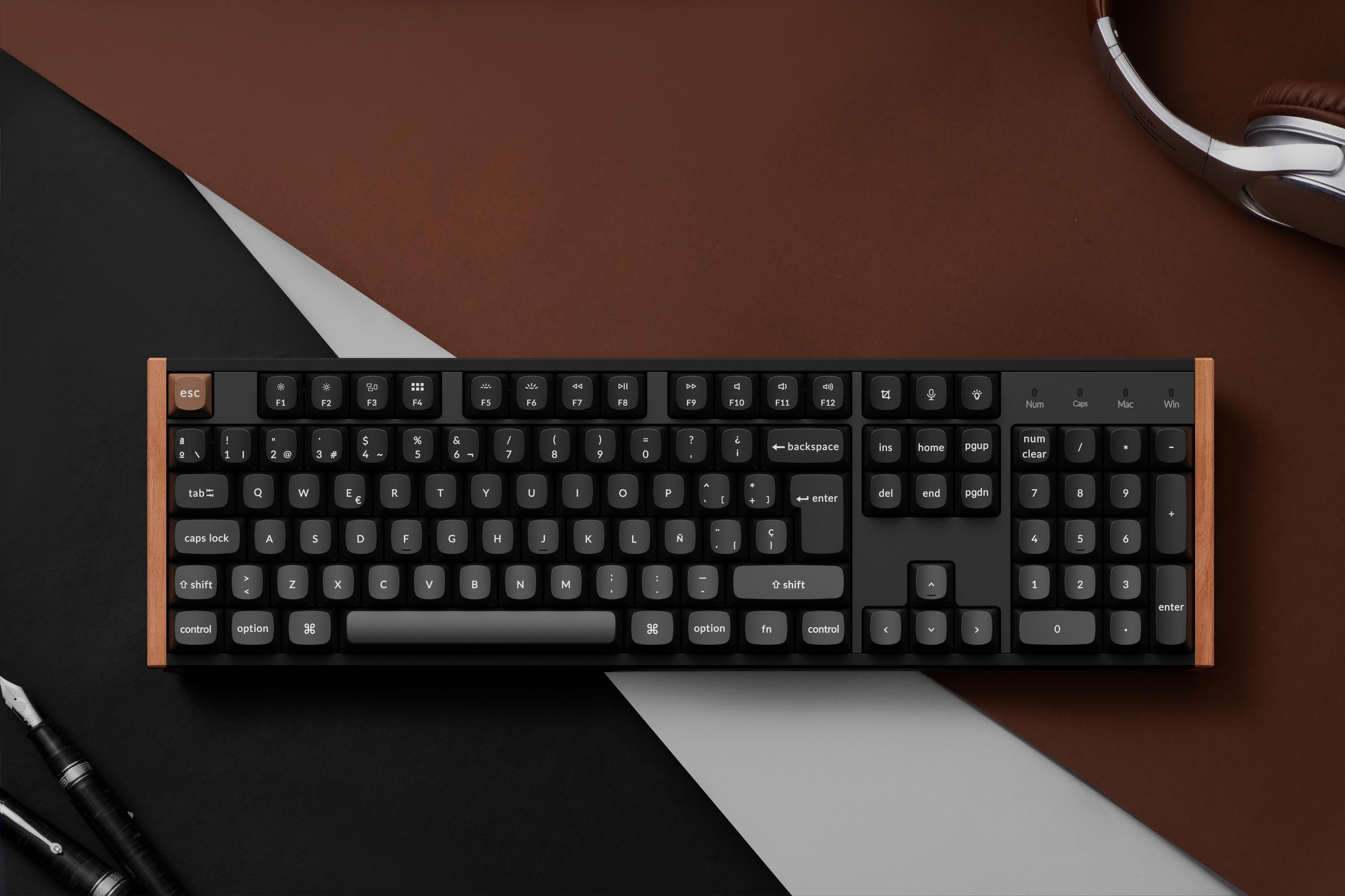 Eine schwarze Tastatur mit Holzrahmen, daneben Kopfhörer und Stifte.