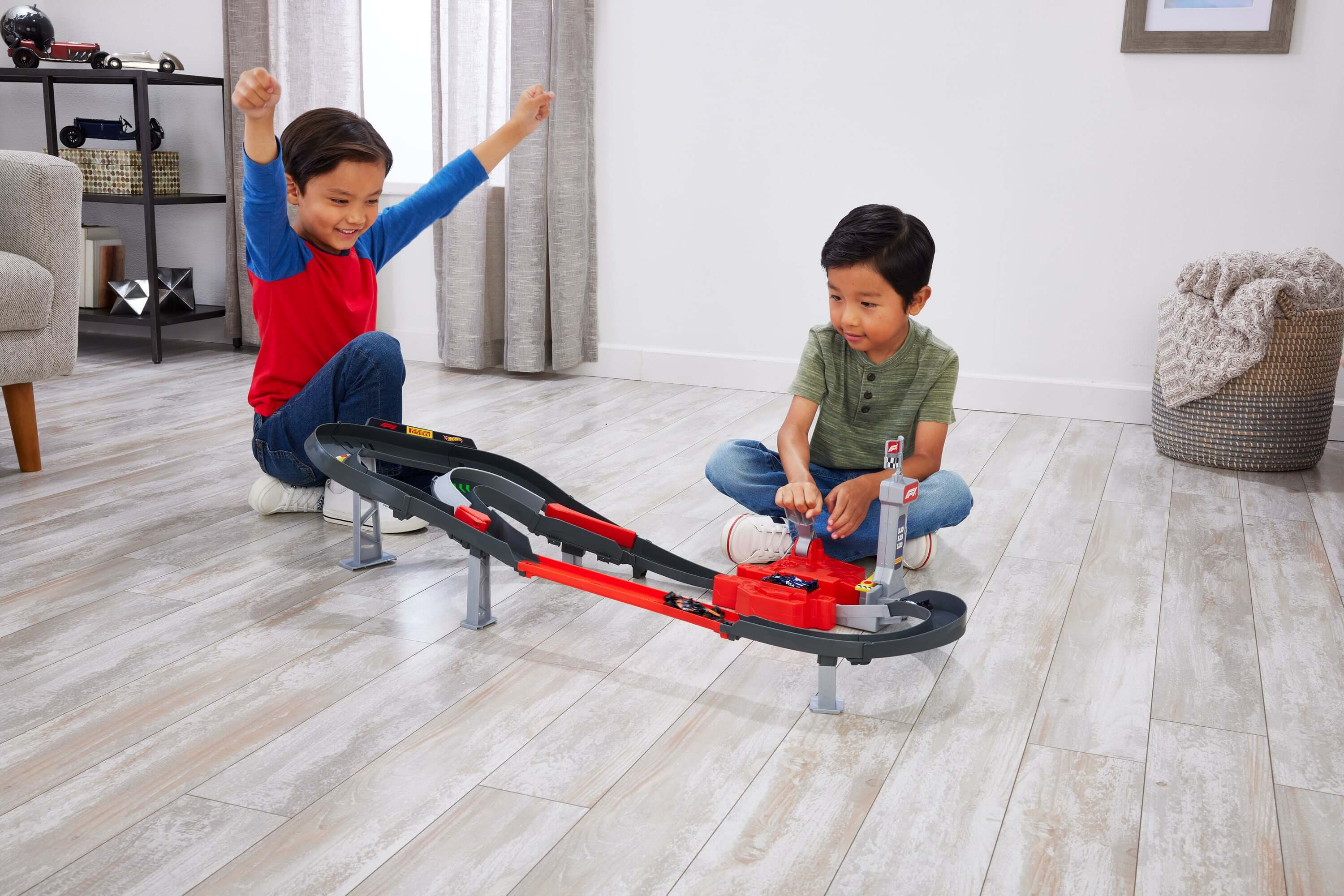 Dos niños juegan con una pista de coches de juguete en un suelo de madera.