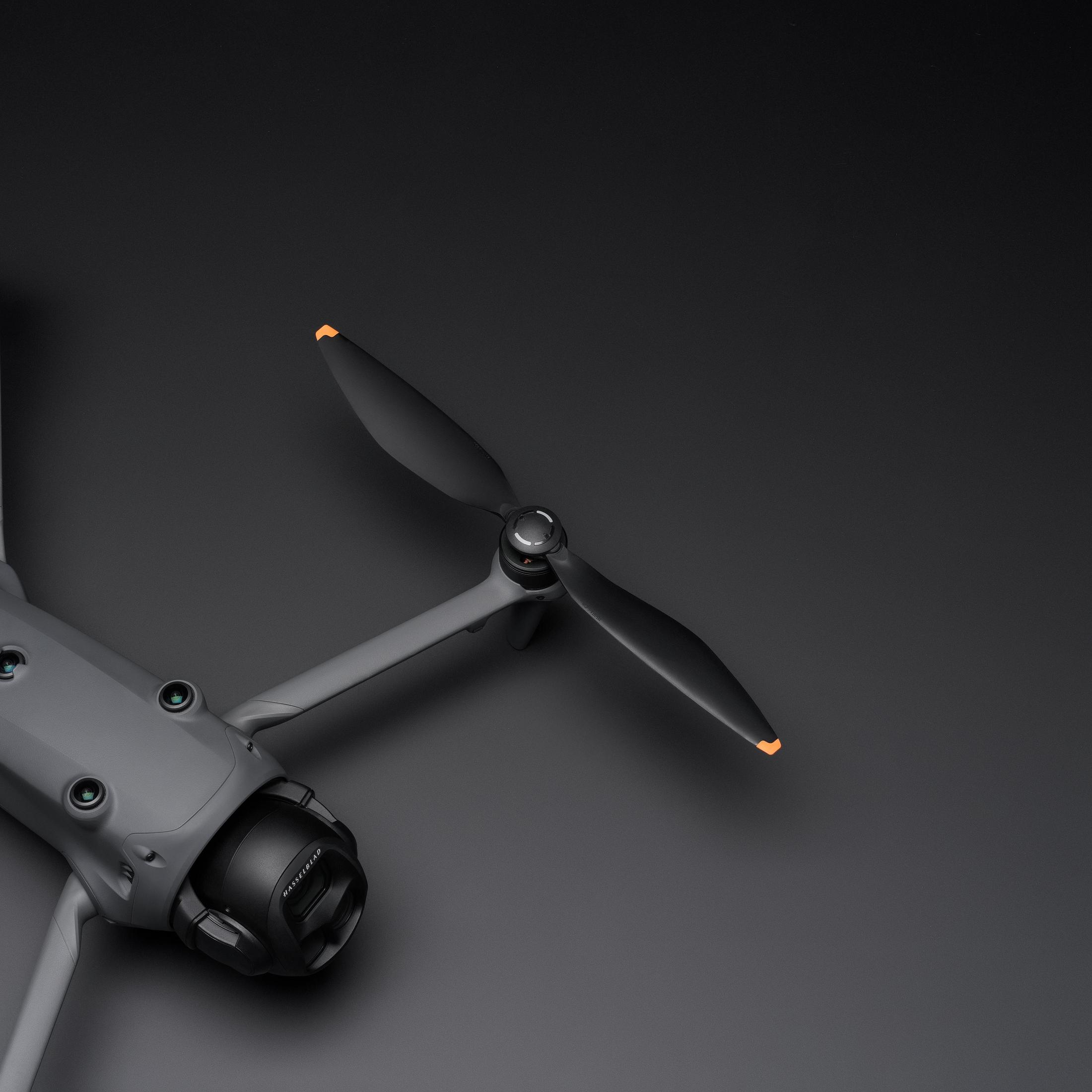 Drone grigio con eliche nere e punte arancioni su sfondo nero.