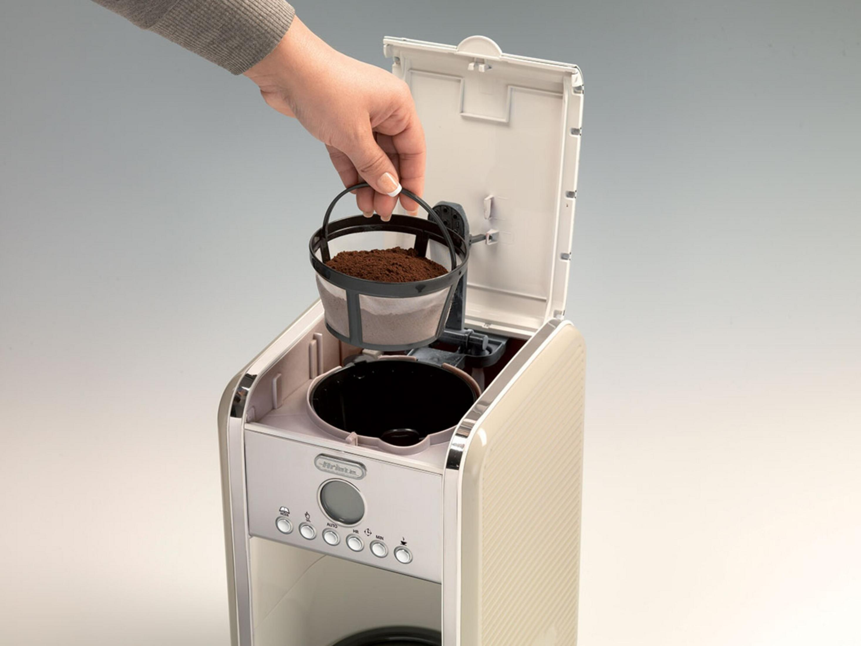 Eine Hand setzt einen Kaffeefilter mit Kaffeepulver in eine Kaffeemaschine ein.