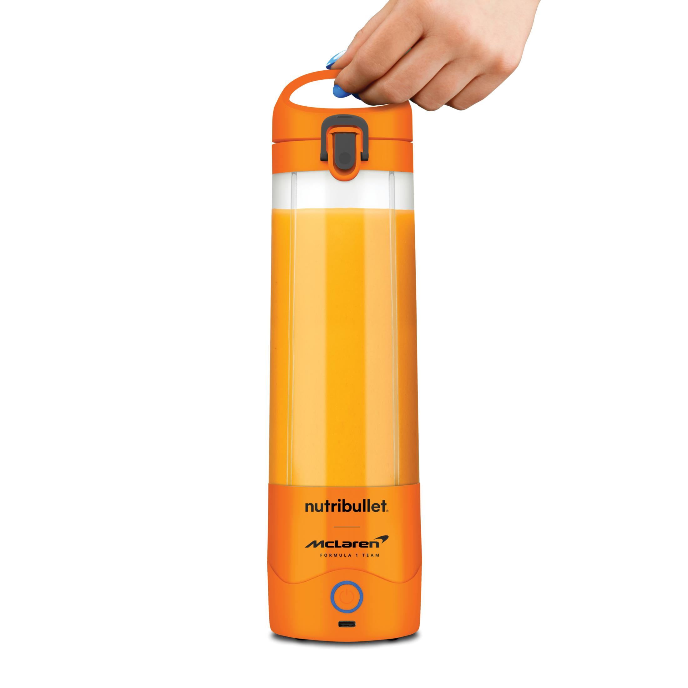 Eine Hand hält einen orangen Nutribullet-Mixer mit orangem Saft.
