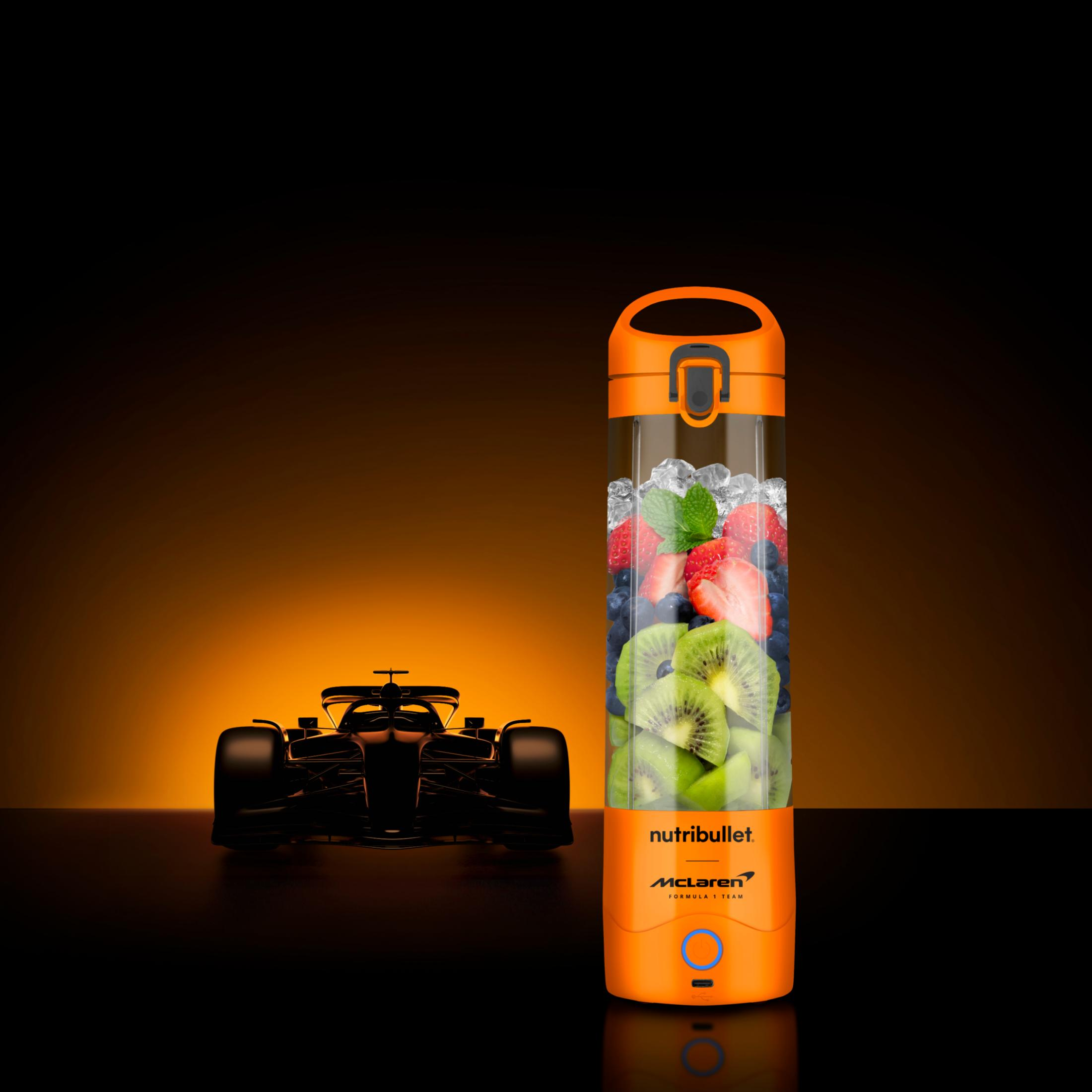 Ein orangefarbener Mixer mit Früchten und Eis neben einem dunklen Rennwagen.