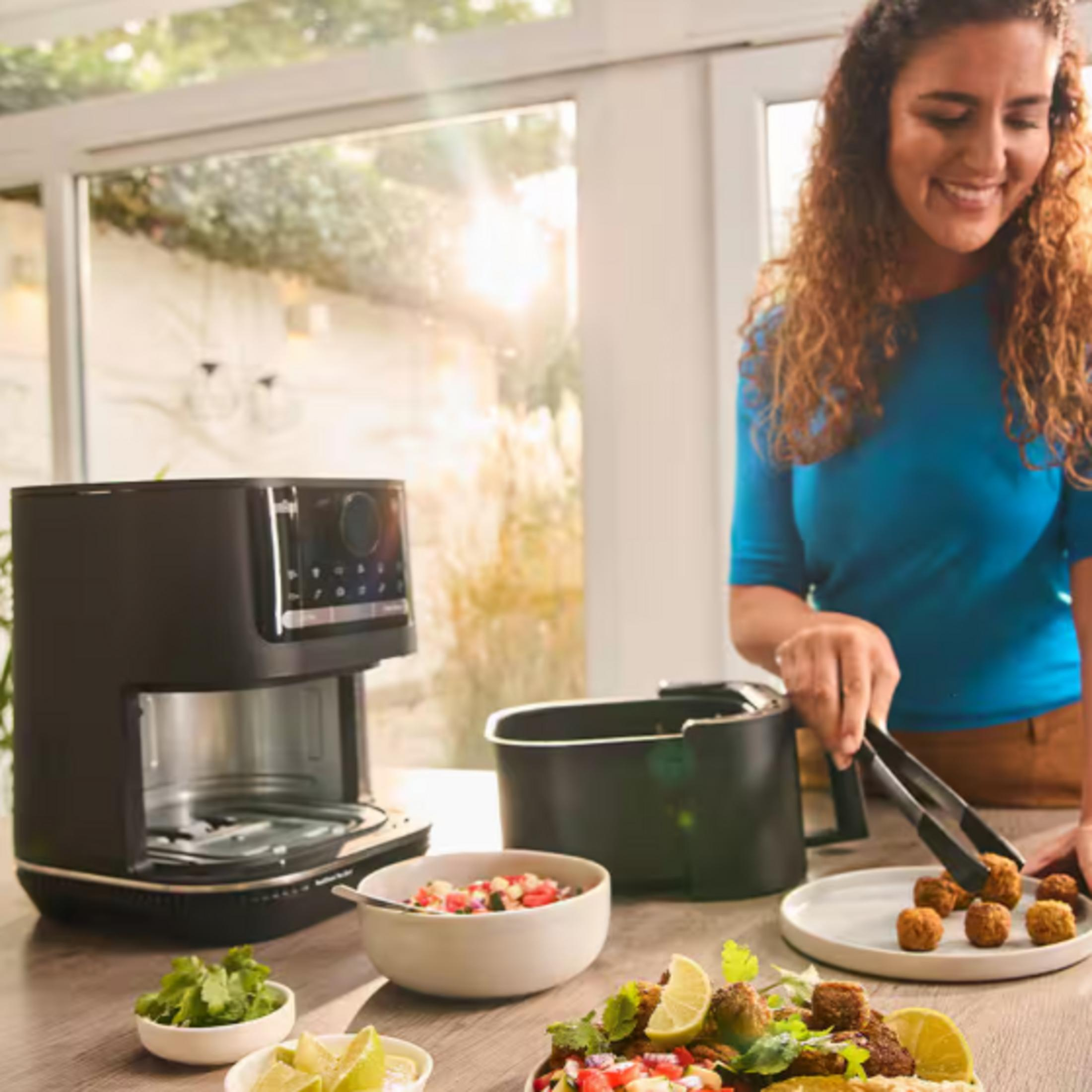 Una donna usa le pinze per mettere falafel su un piatto accanto a una friggitrice ad aria.
