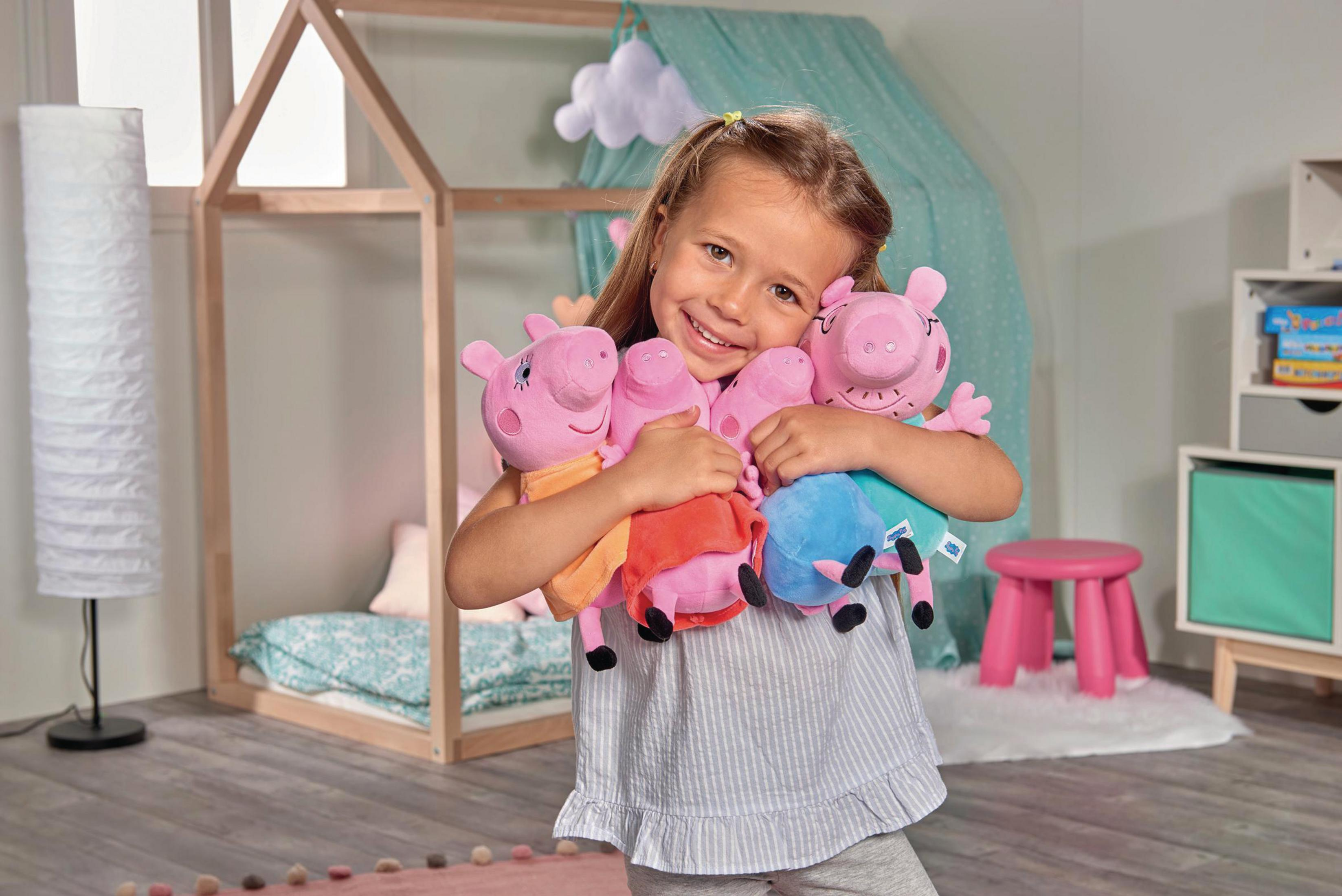 Ein lachendes Mädchen umarmt mehrere Peppa Wutz Plüschtiere in einem Kinderzimmer.