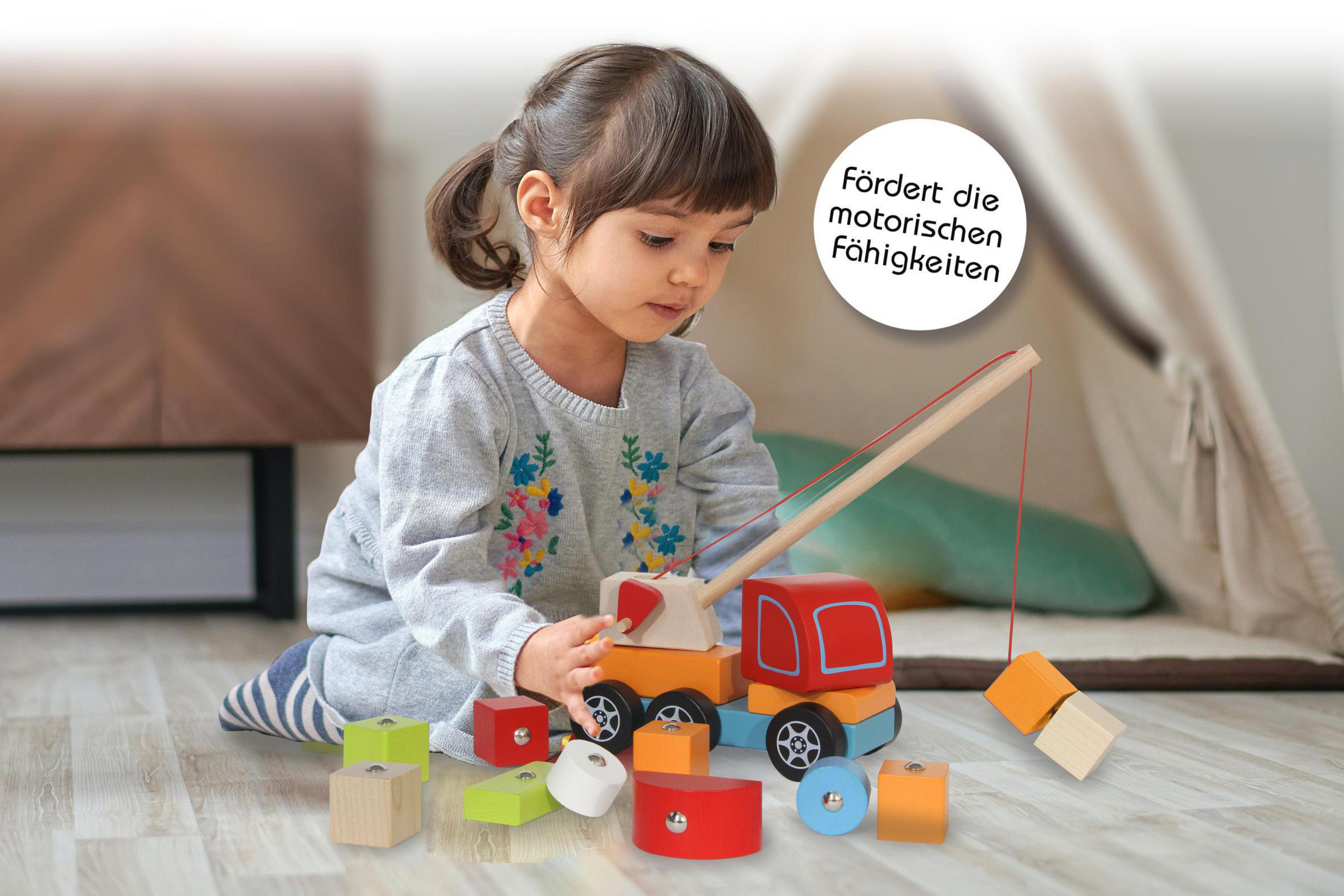 Ein kleines Mädchen spielt mit einem Holzbaukran und bunten Holzklötzen.