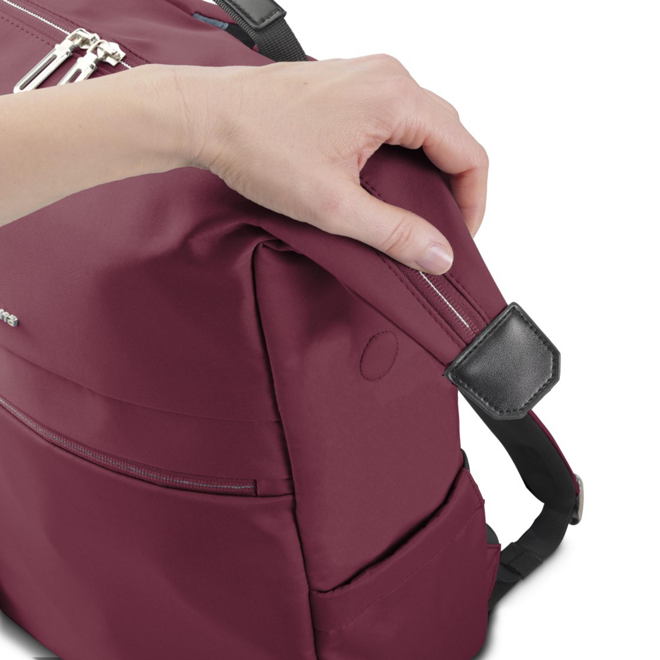 Una mano afferra una borsa color bordeaux con cerniere. Si vede una cinghia nera.