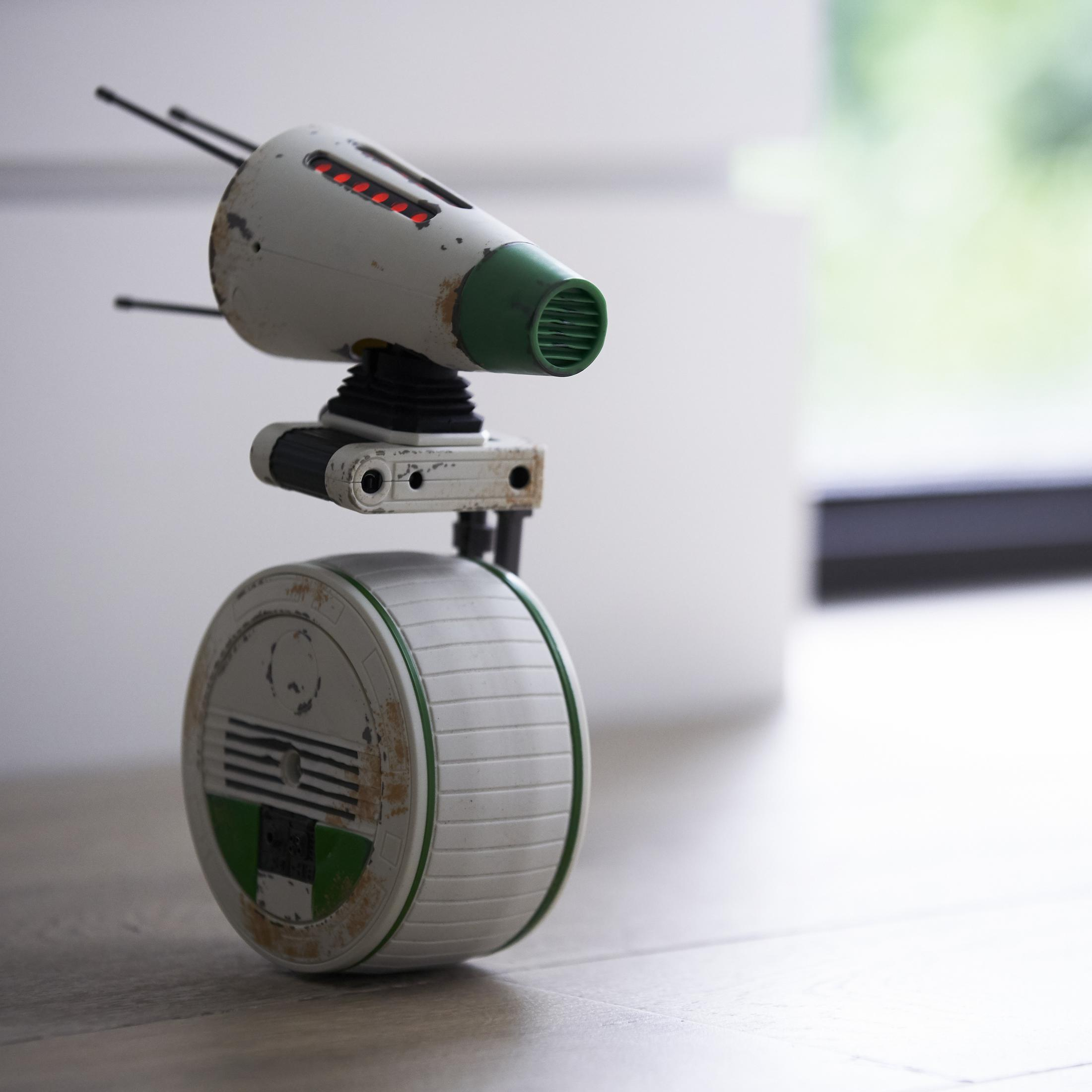 Ein weißer Roboter mit Rad steht auf einem Holzboden.