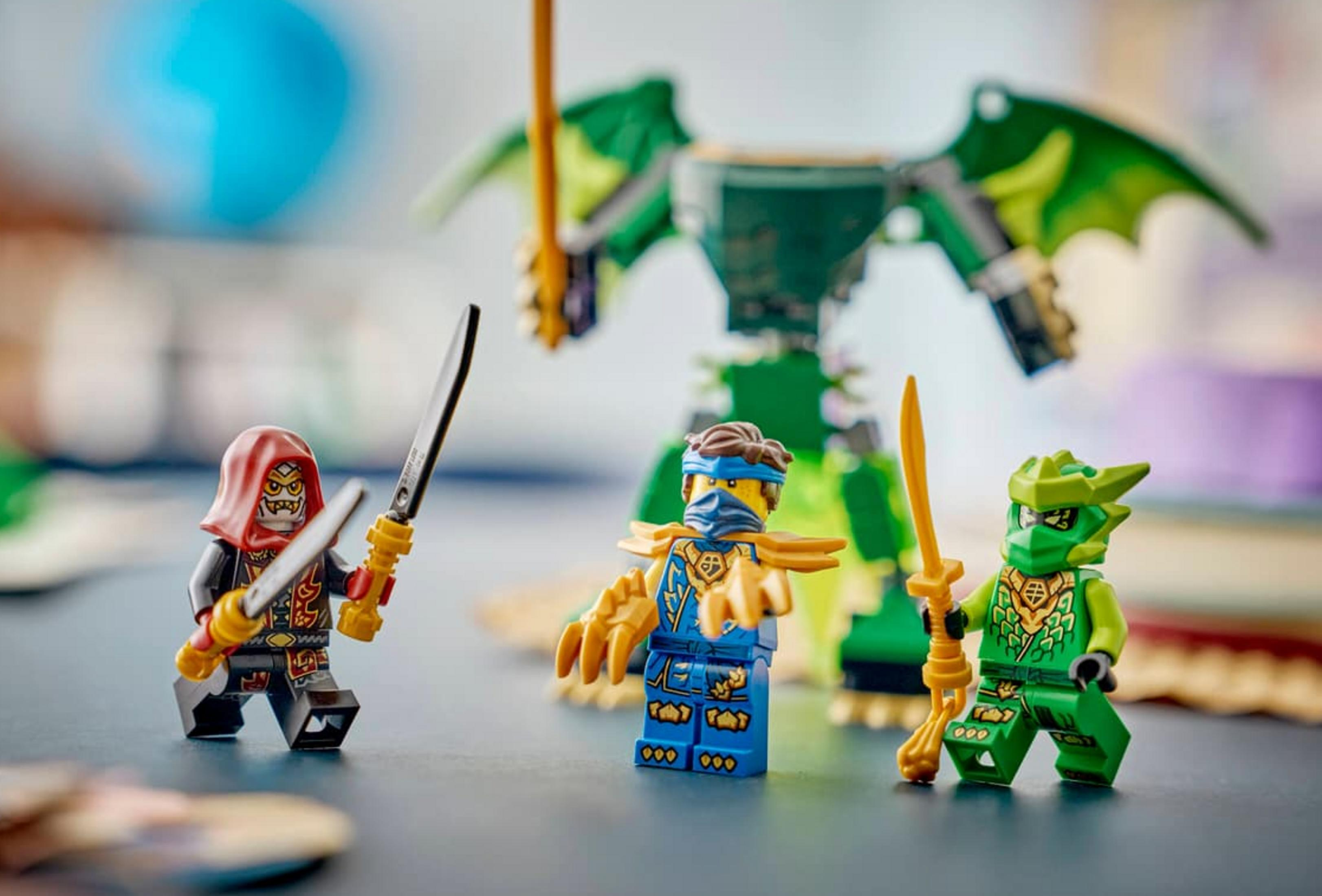 Tres figuras de Ninjago con armas frente a un juguete de dragón verde.