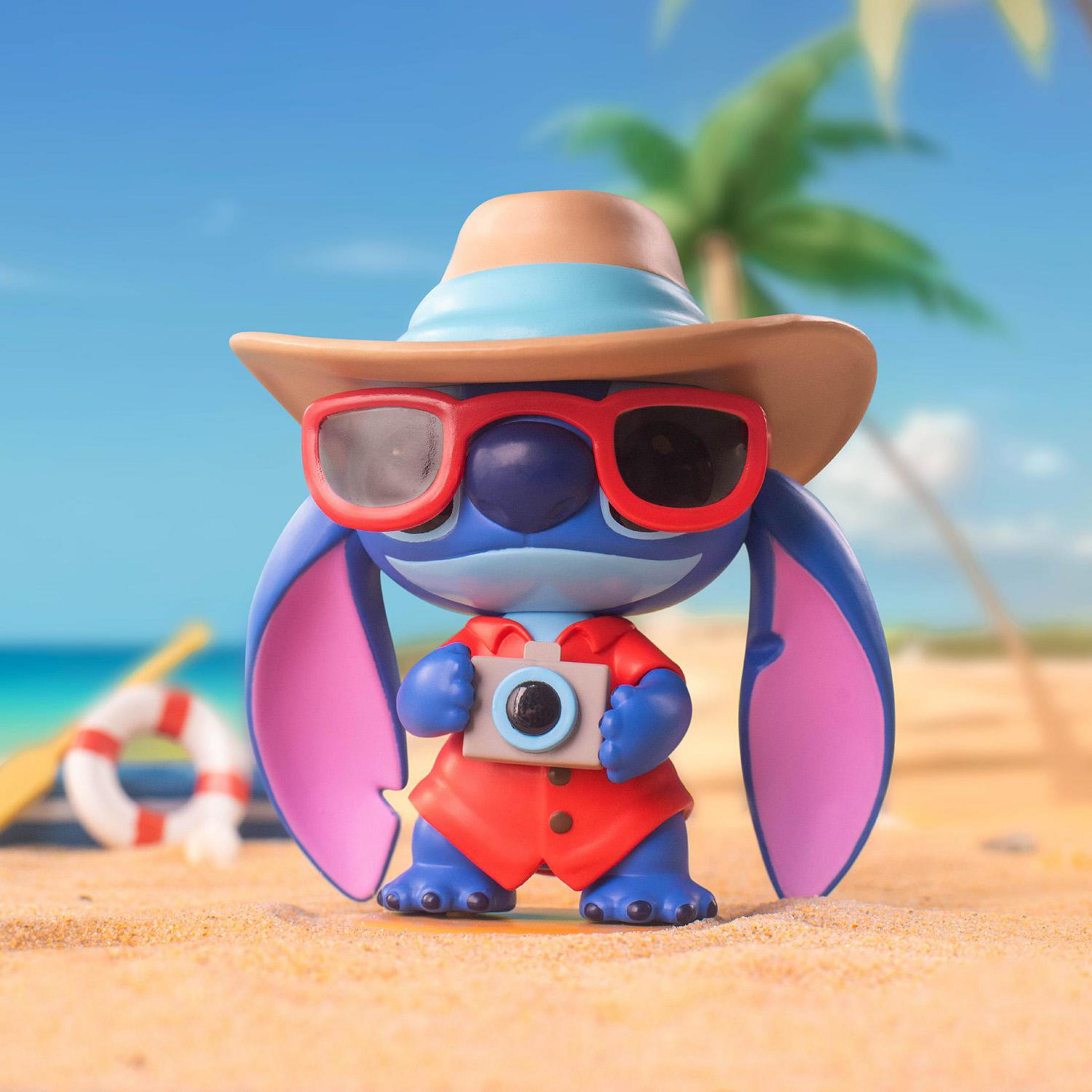 Eine Stitch-Figur mit Hut und Sonnenbrille hält eine Kamera am Strand.