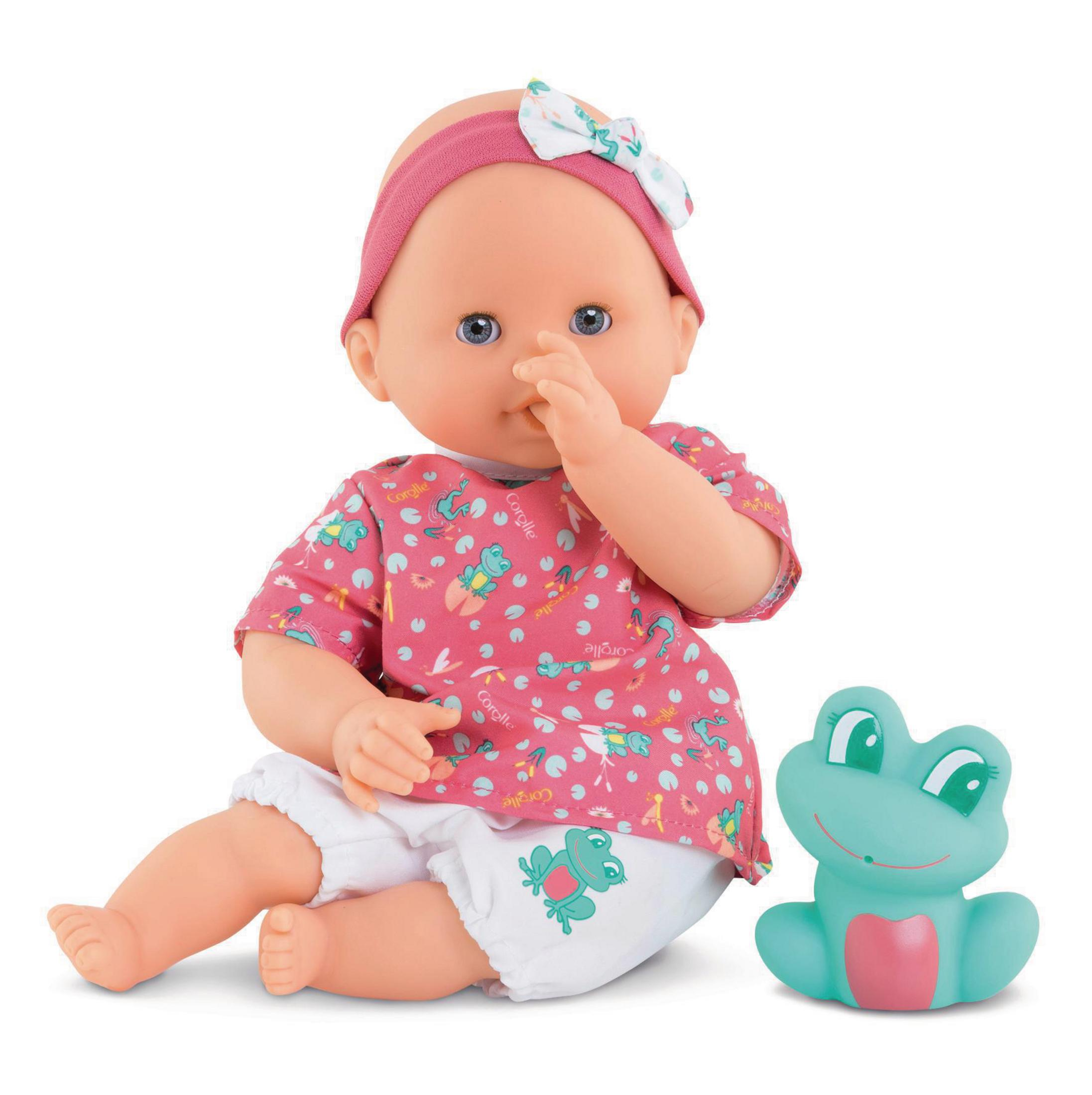 Baby-Puppe in rosa Hemd mit Fröschen, sitzt neben einem grünen Froschspielzeug.