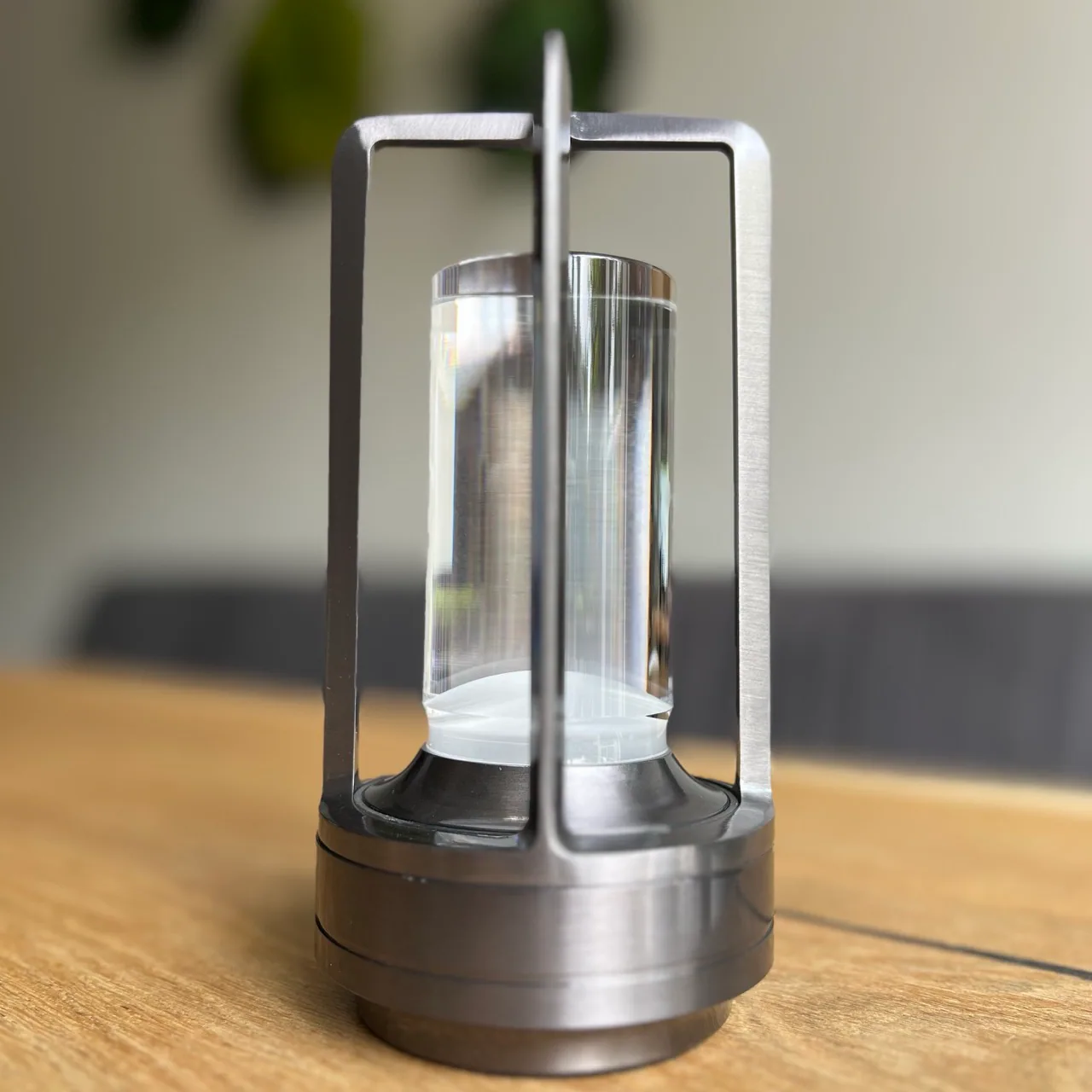 Moderne metallische Laterne mit klarem Glaszylinder auf Holztisch.
