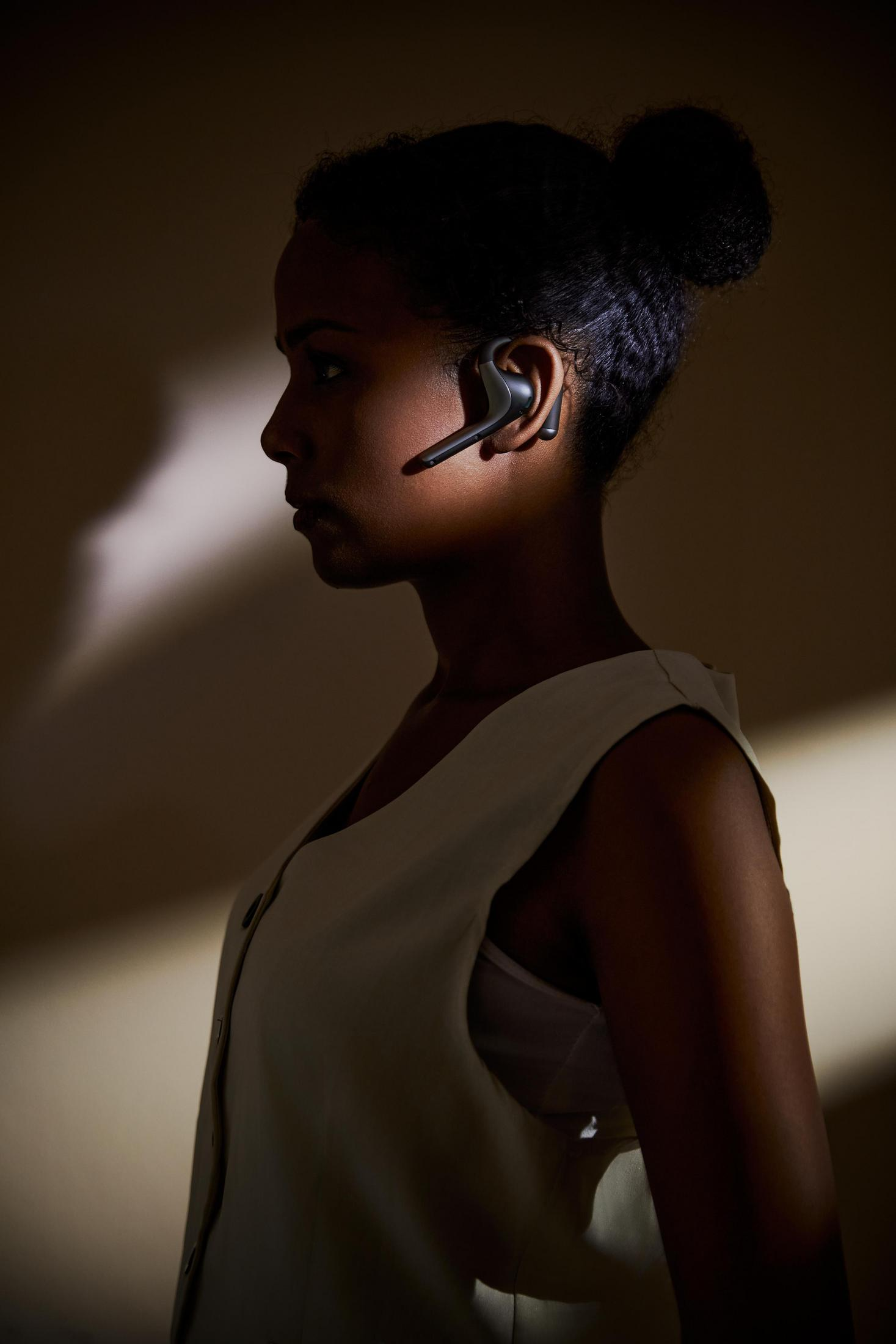 Donna di profilo con auricolare, sfondo scuro con riflesso.
