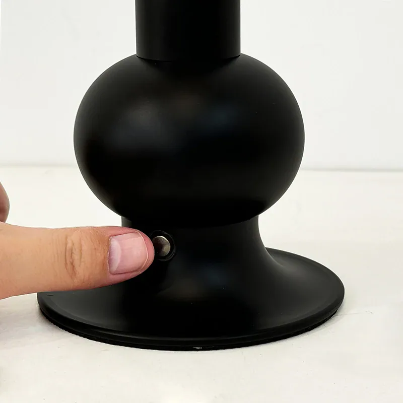 Ein Finger drückt auf einen kleinen Knopf an der Basis einer schwarzen Lampe.