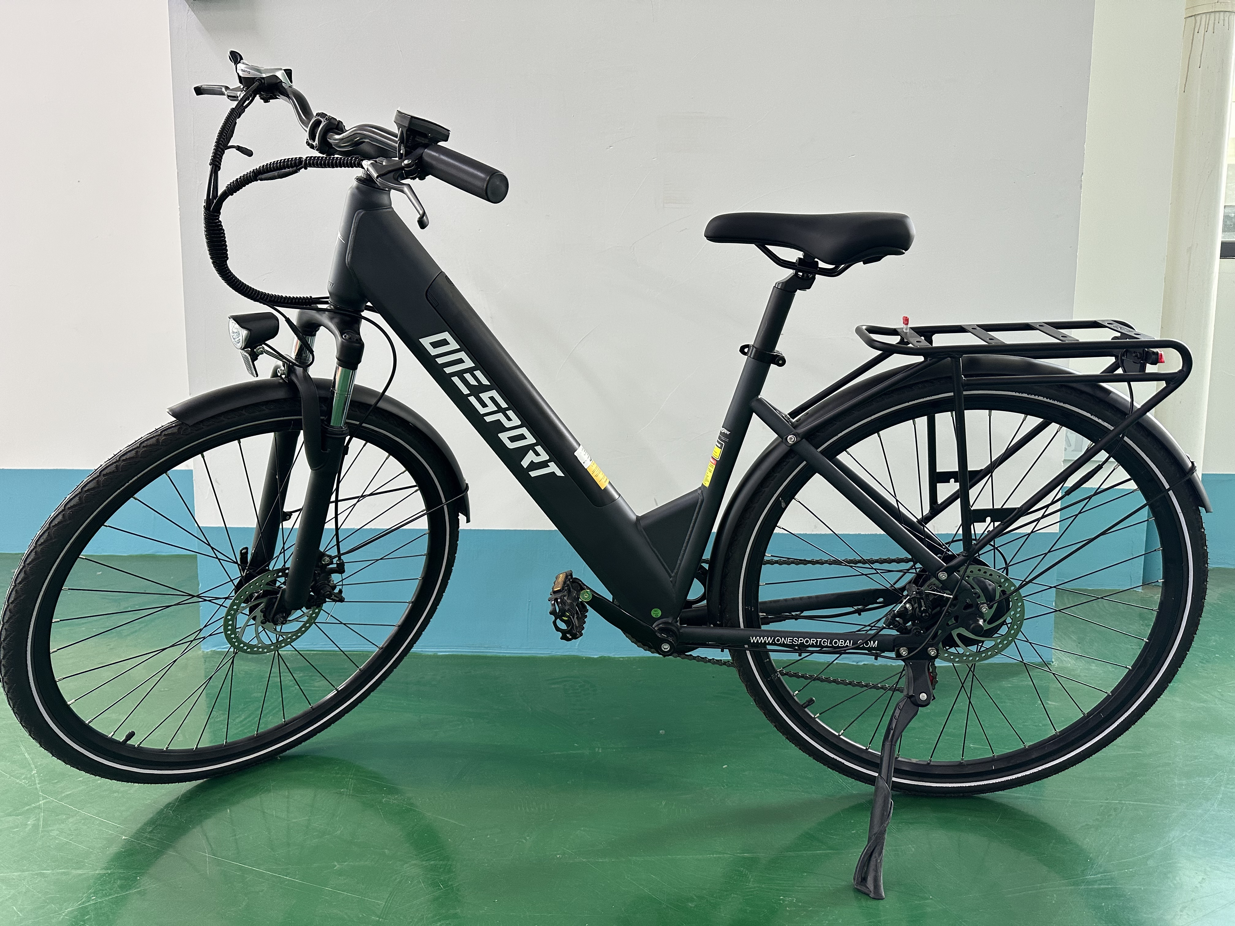 Ein schwarzes E-Bike mit Gepäckträger steht auf einem grünen Boden.