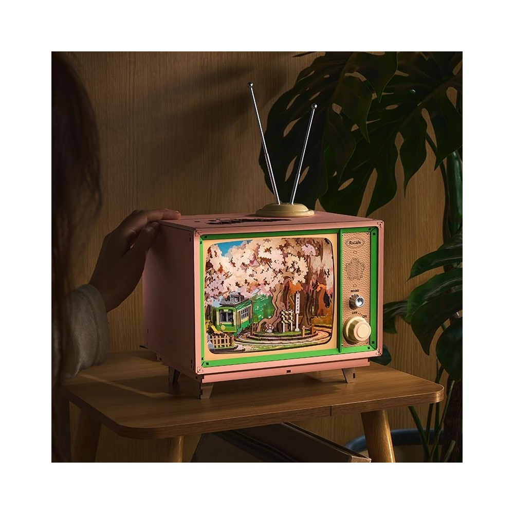 Kiraz çiçeği ağacı, tren ve ev dioraması gösteren pembe retro TV.