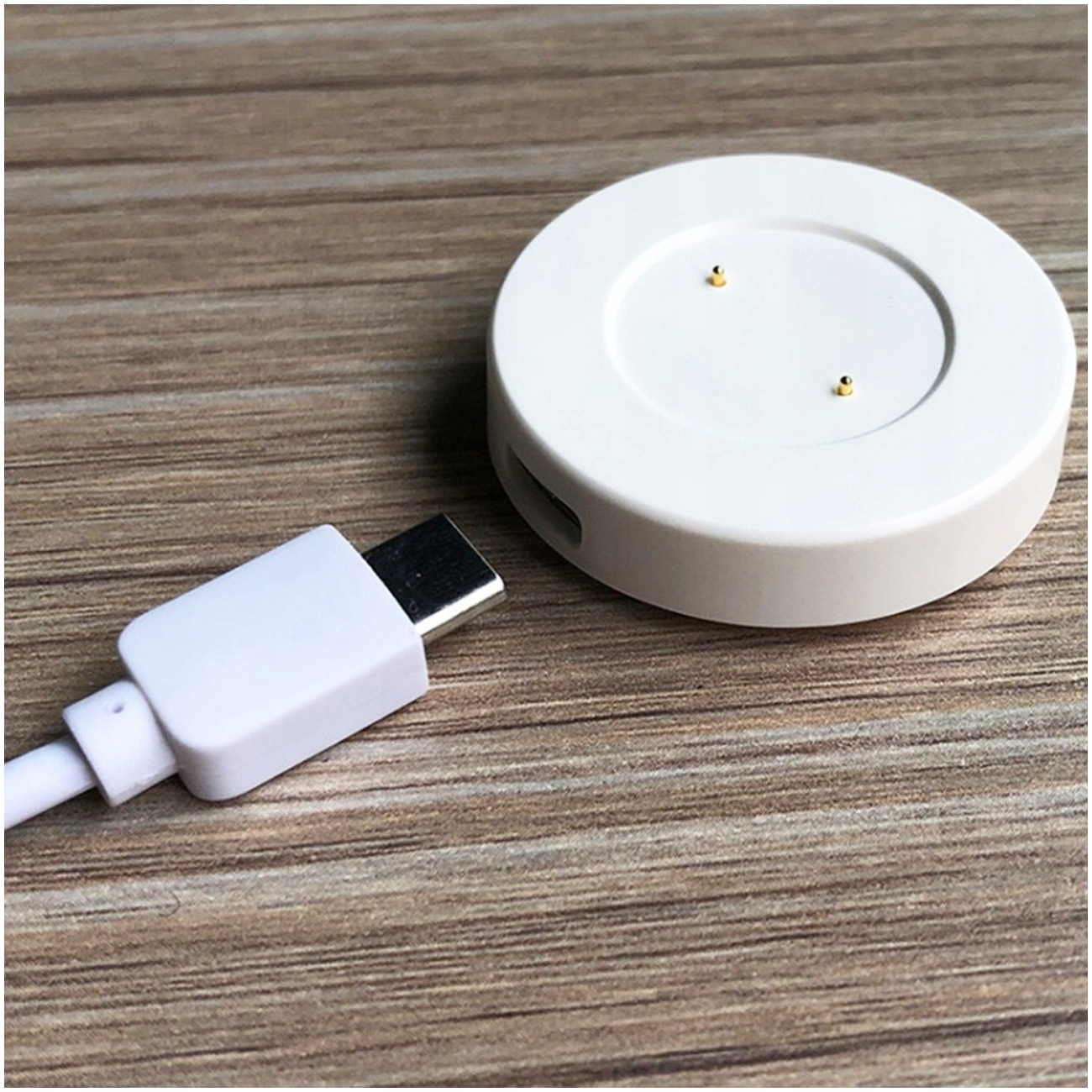 Biały kabel USB-C leży obok okrągłej białej ładowarki na drewnie.