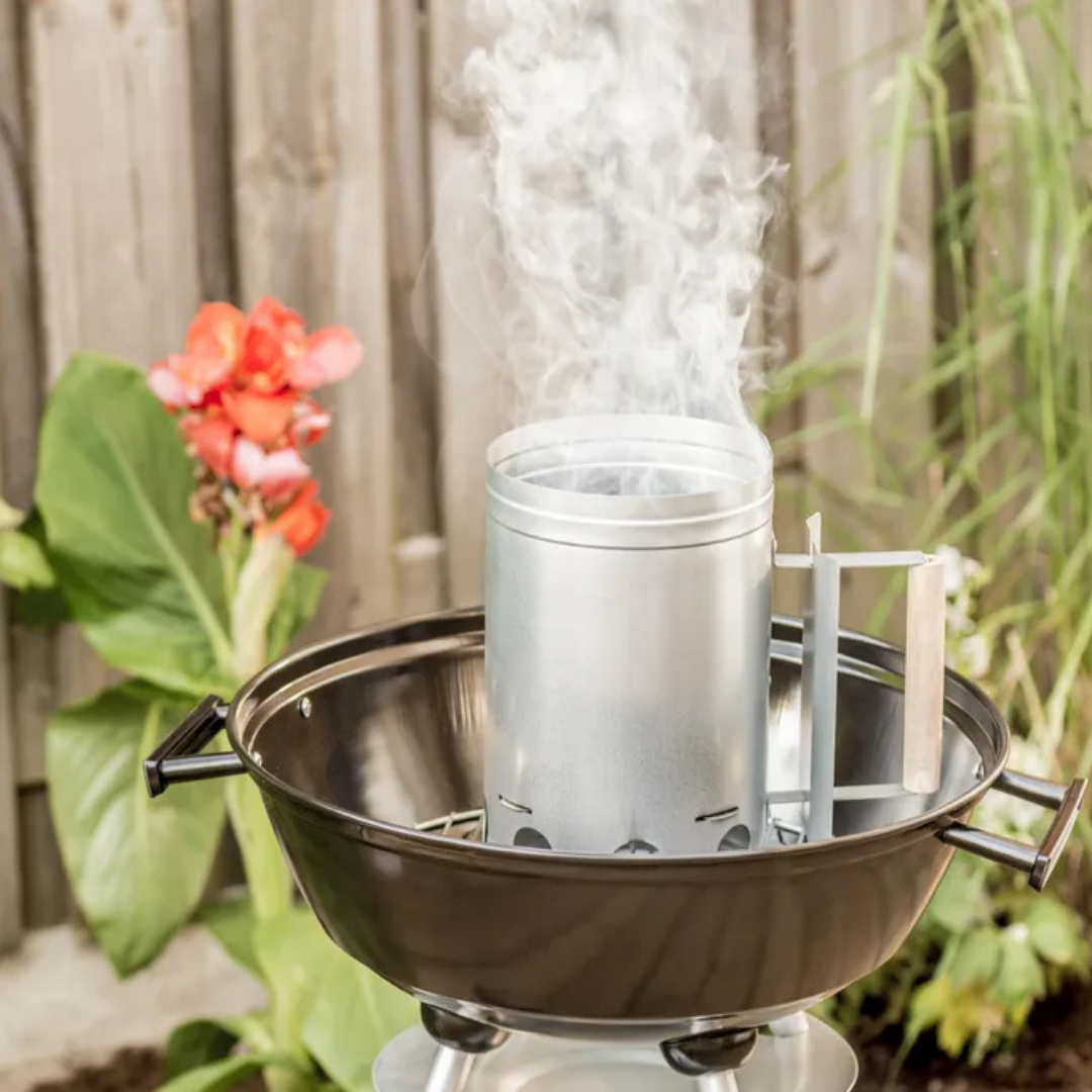 Ein voller Rauchkaminstarter sitzt in einem schwarzen Grill, mit Blumen und Holzzaun.