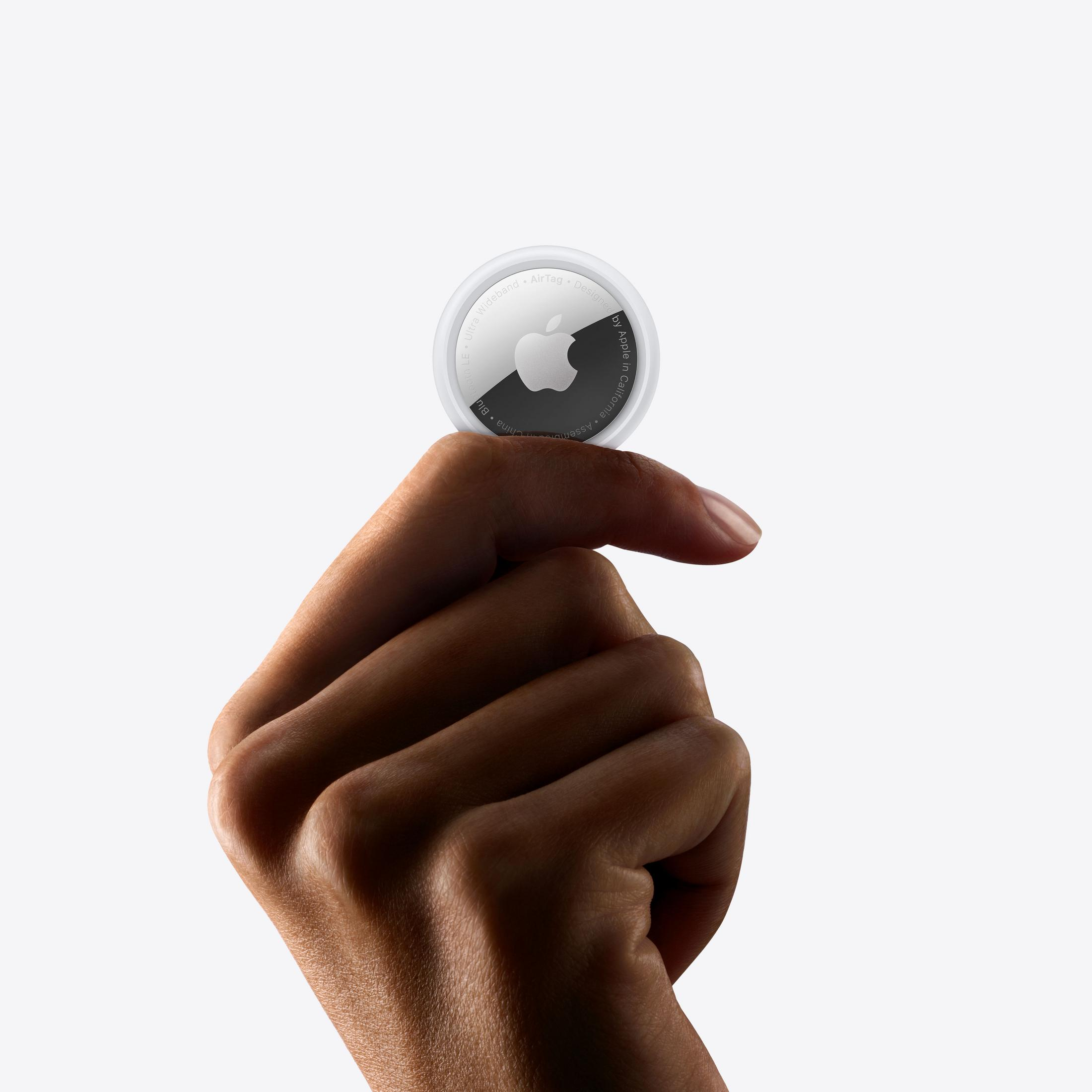Una mano sostiene un Apple AirTag blanco redondo con un logo de Apple plateado.