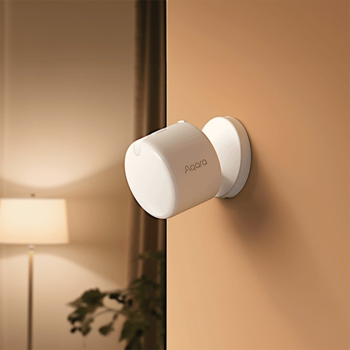 Ein weißes Aqara-Gerät ist an einer Wand montiert. Links ist eine Lampe zu sehen.