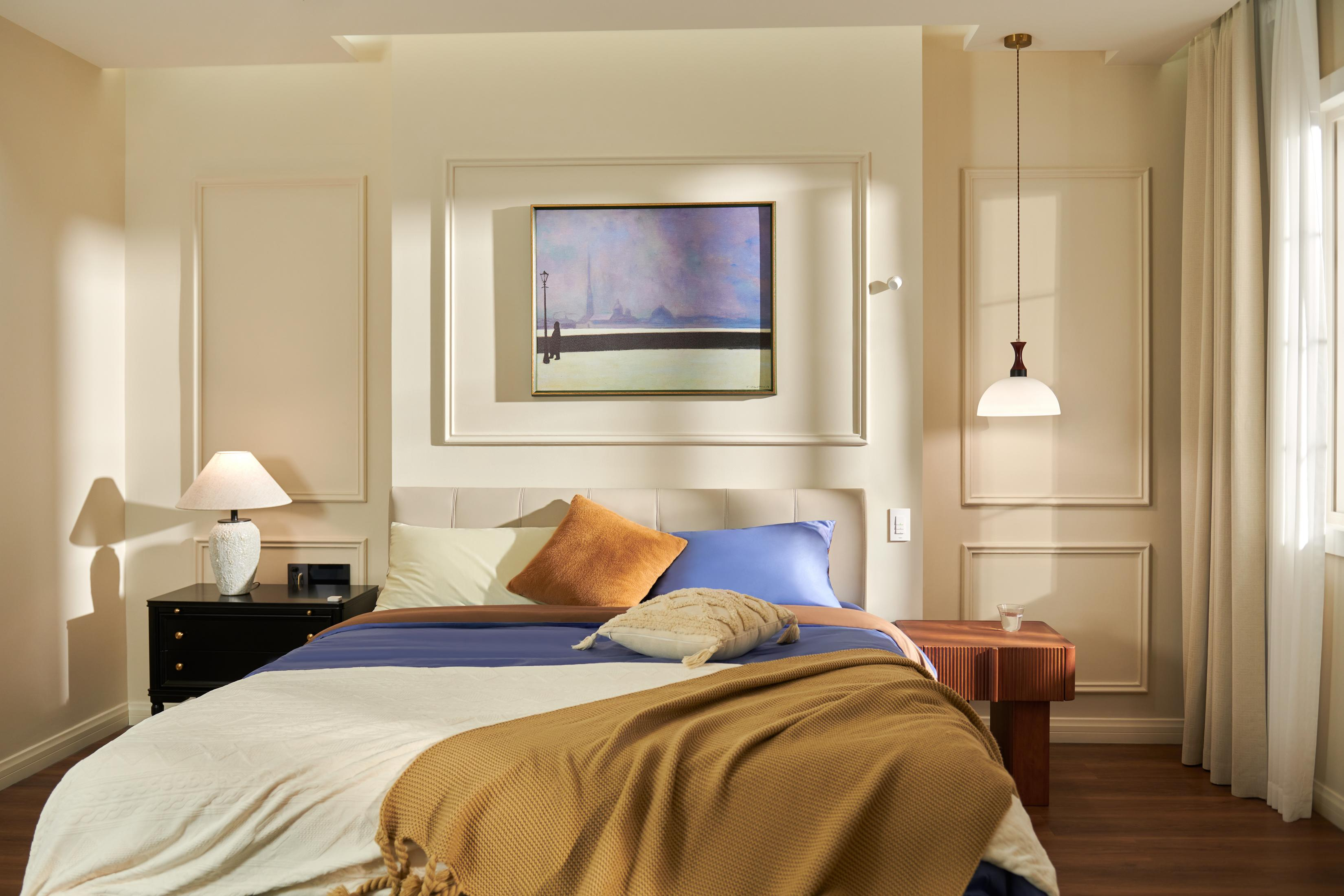 Ein Schlafzimmer mit einem Bett, das mit Kissen und Decken geschmückt ist. Ein Gemälde hängt über dem Bett.