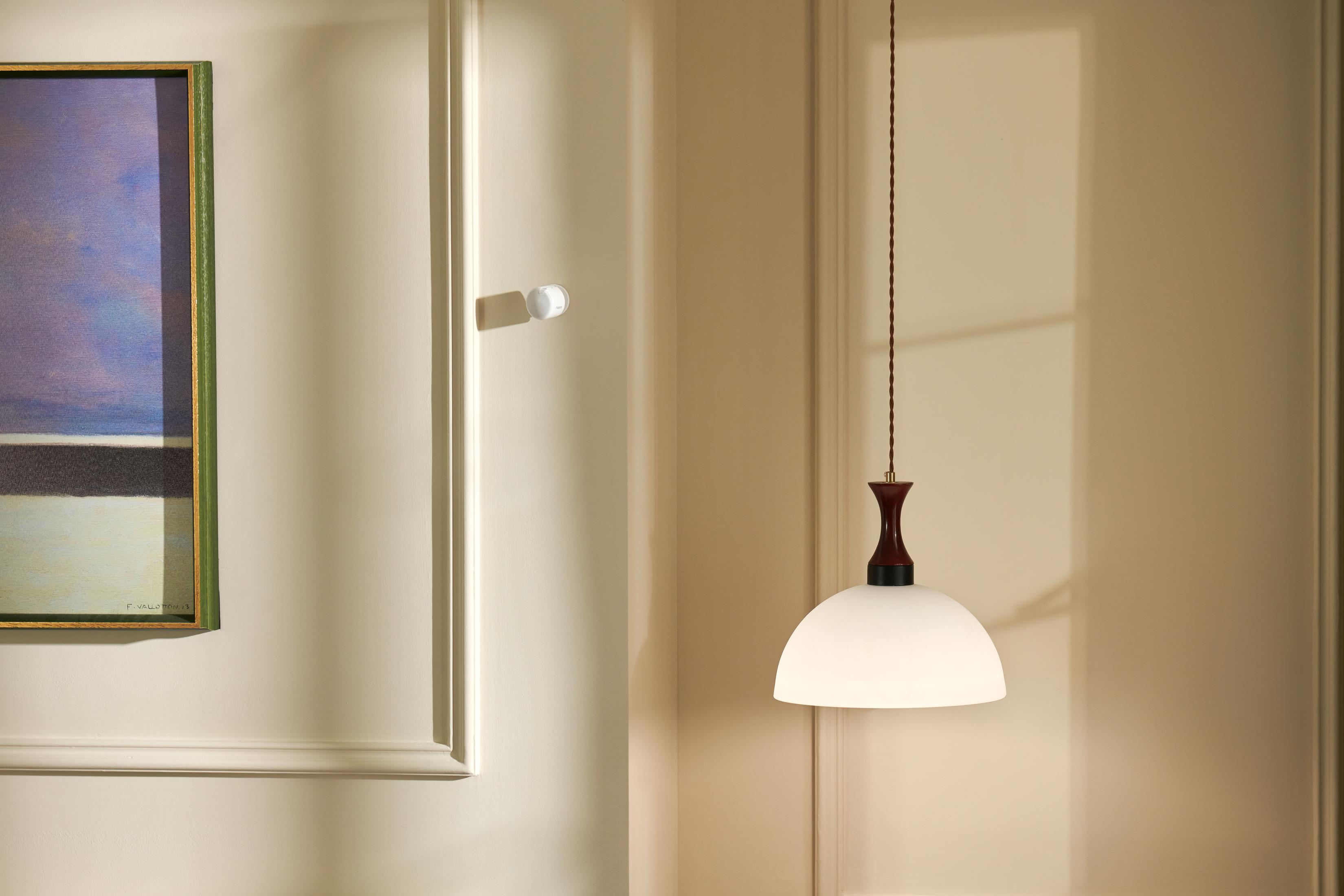 Eine Pendelleuchte mit weißem Glasschirm und dunklem Holzdetail hängt neben einem Gemälde.