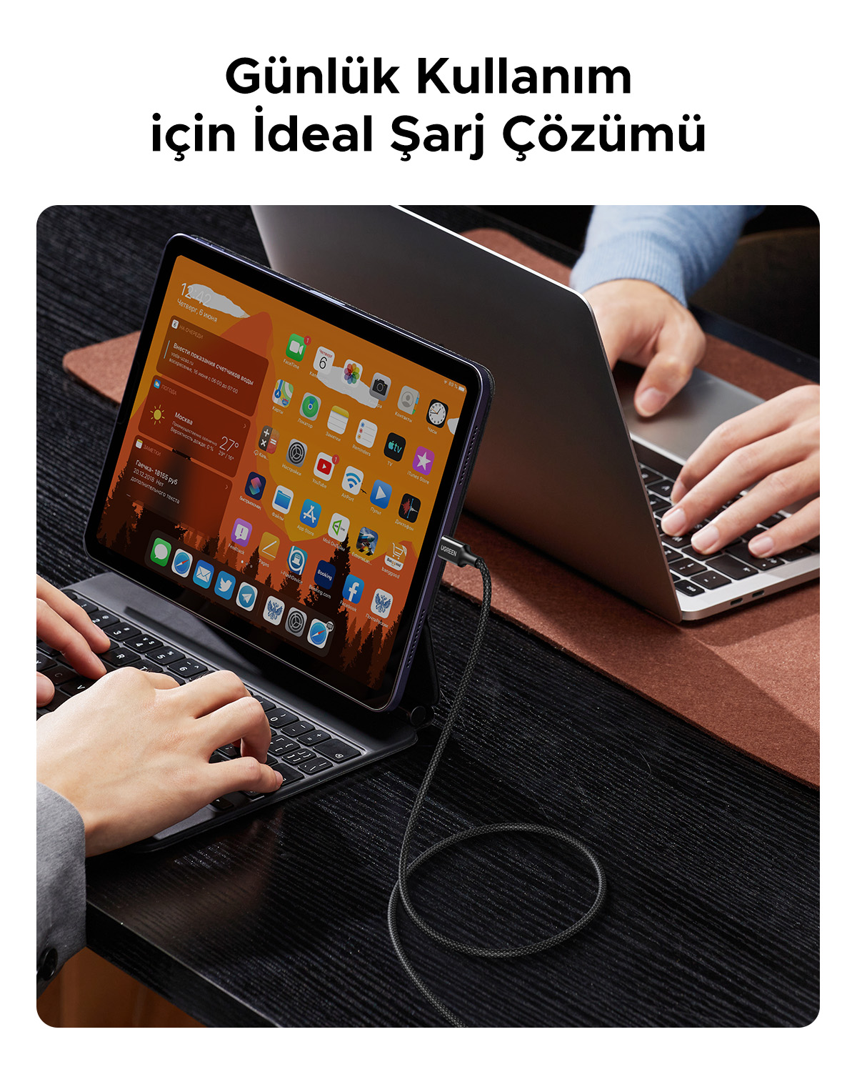 Bir kişi, şarj olan bağlı bir tabletiyle klavyede yazıyor.