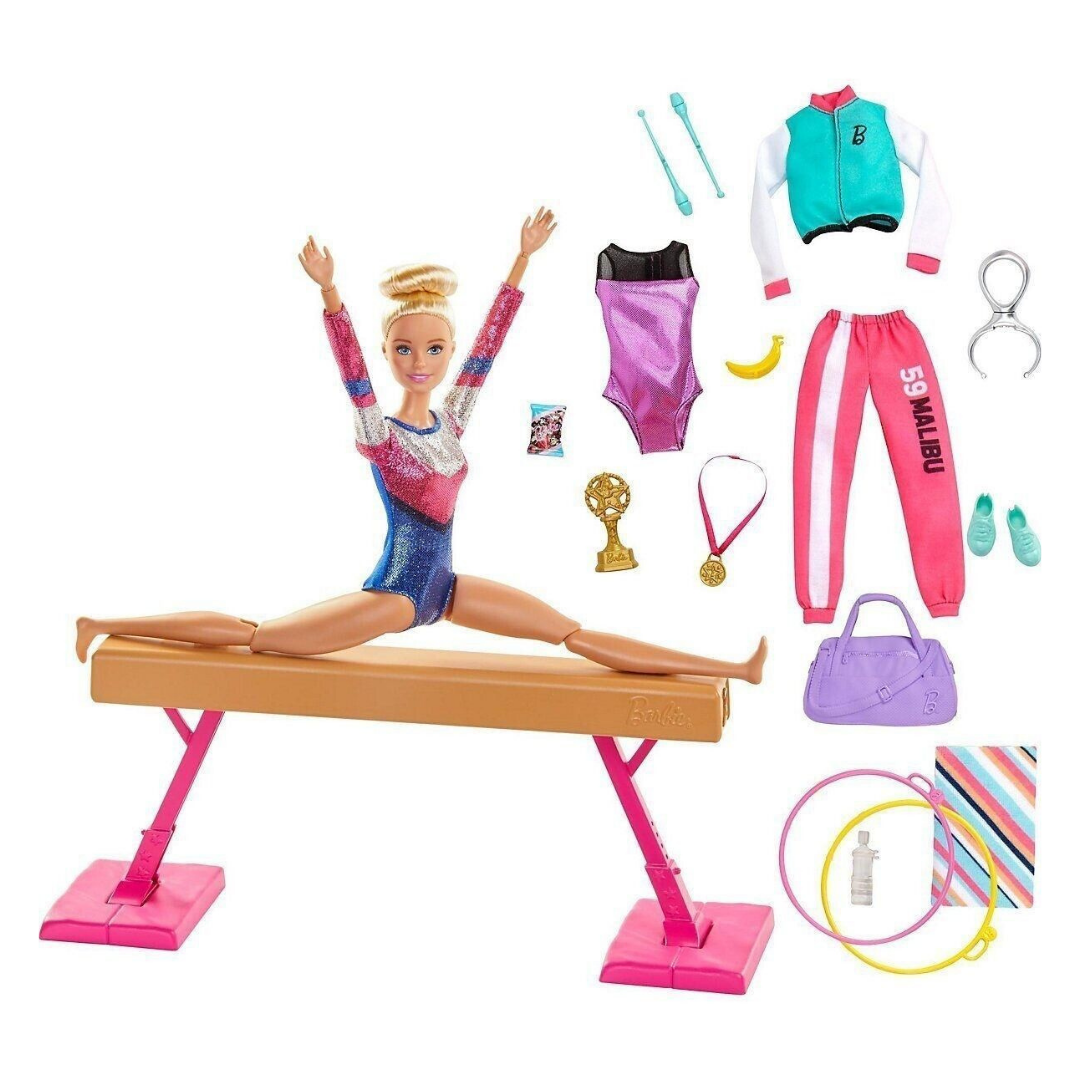 Barbie auf einem Schwebebalken, umgeben von Turnkleidung und Accessoires.