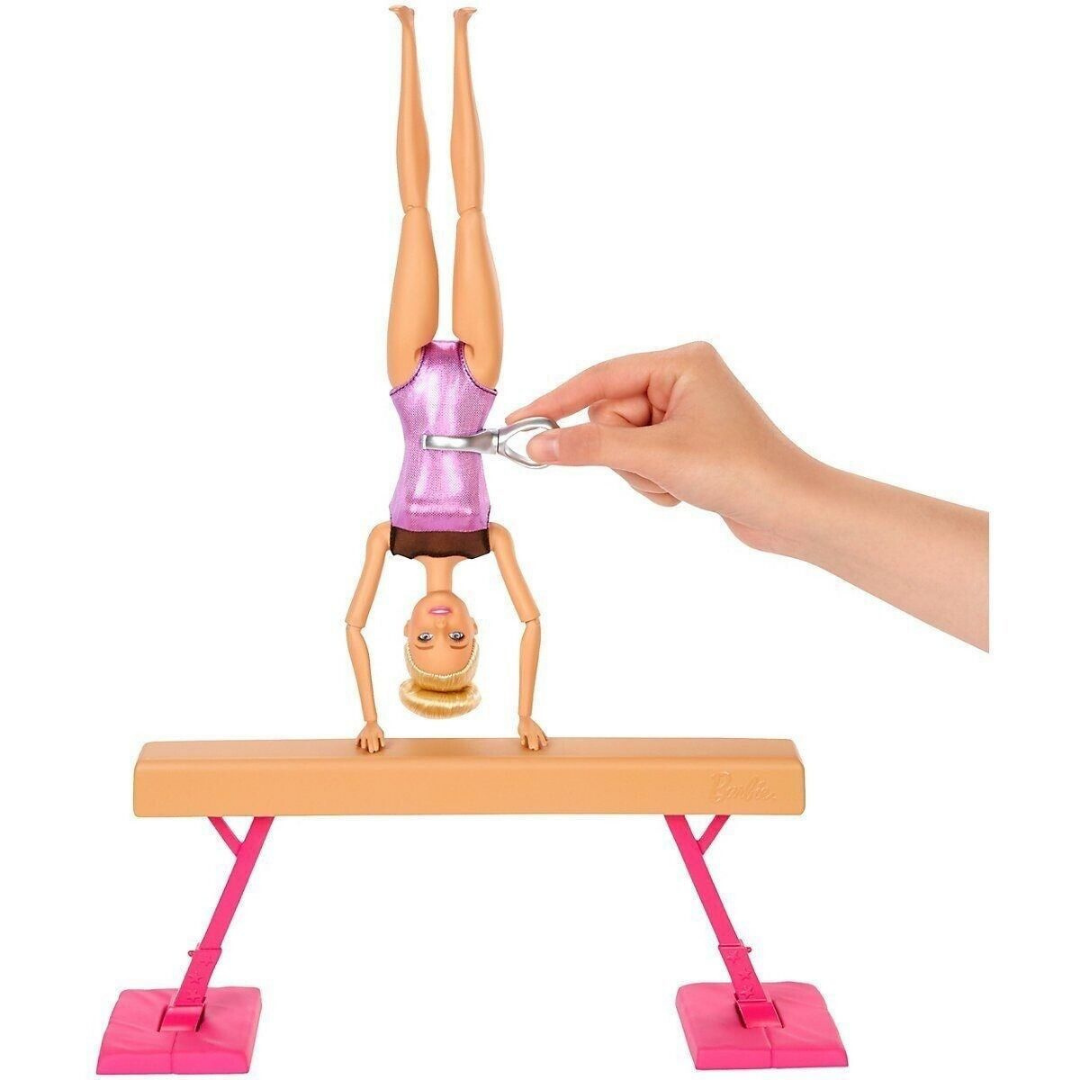 Barbie-Puppe macht einen Handstand auf einem Schwebebalken mit einem silbernen Aufziehschlüssel.
