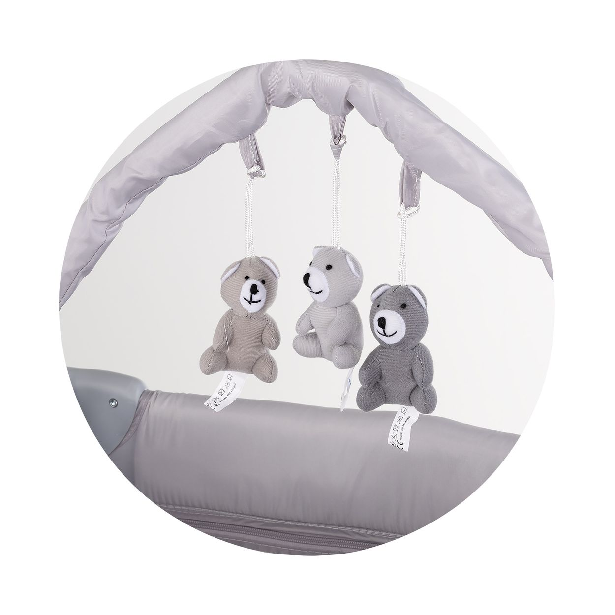 Drei graue Teddybären hängen an einer Spieluhr über einem Kinderbett.
