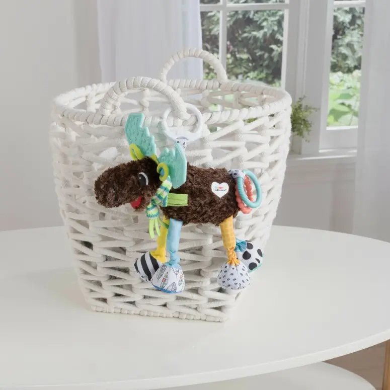 Un peluche de alce con patas de colores cuelga de una cesta blanca.