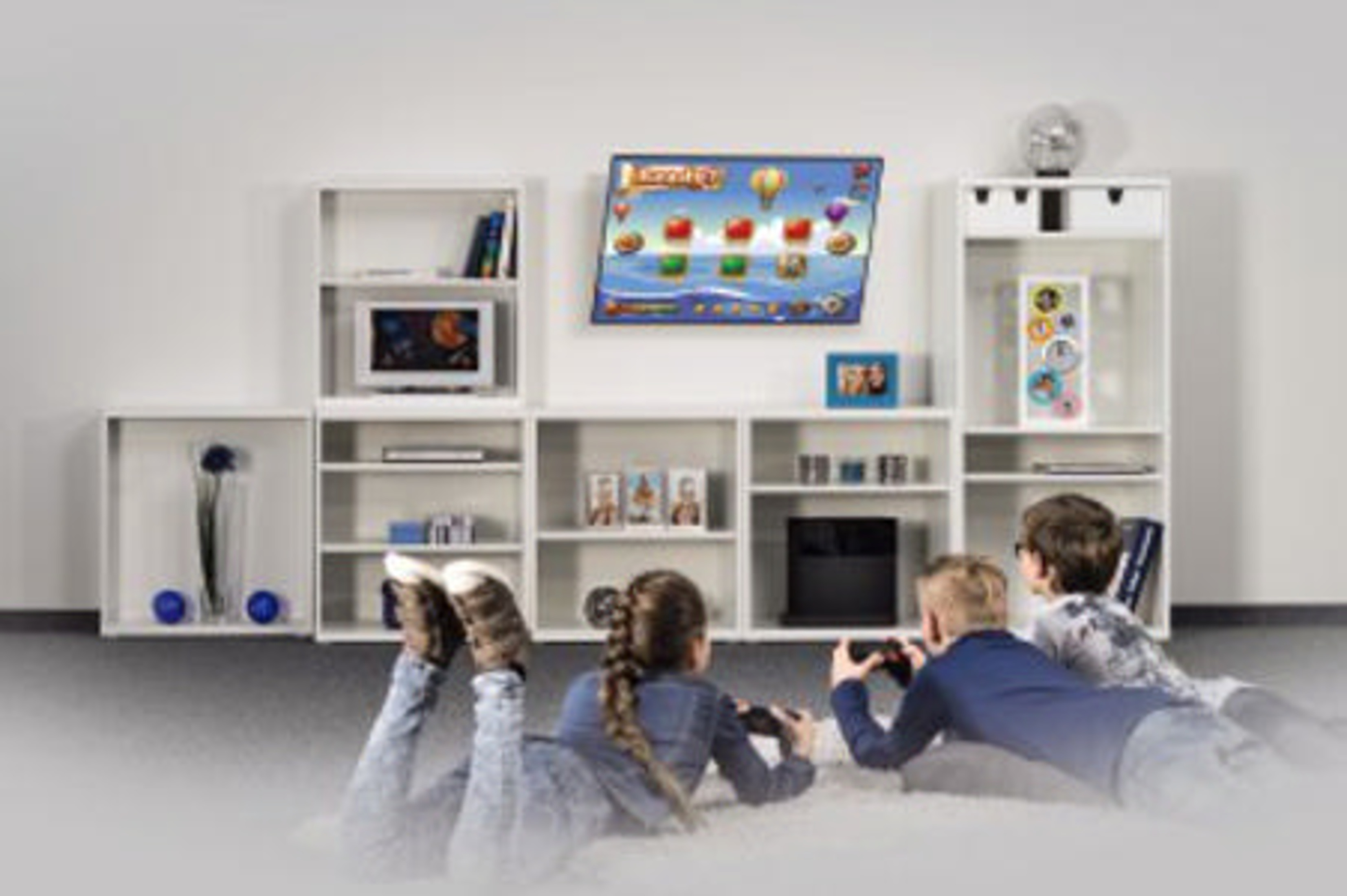 Tres niños tumbados juegan videojuegos en una pantalla de TV.