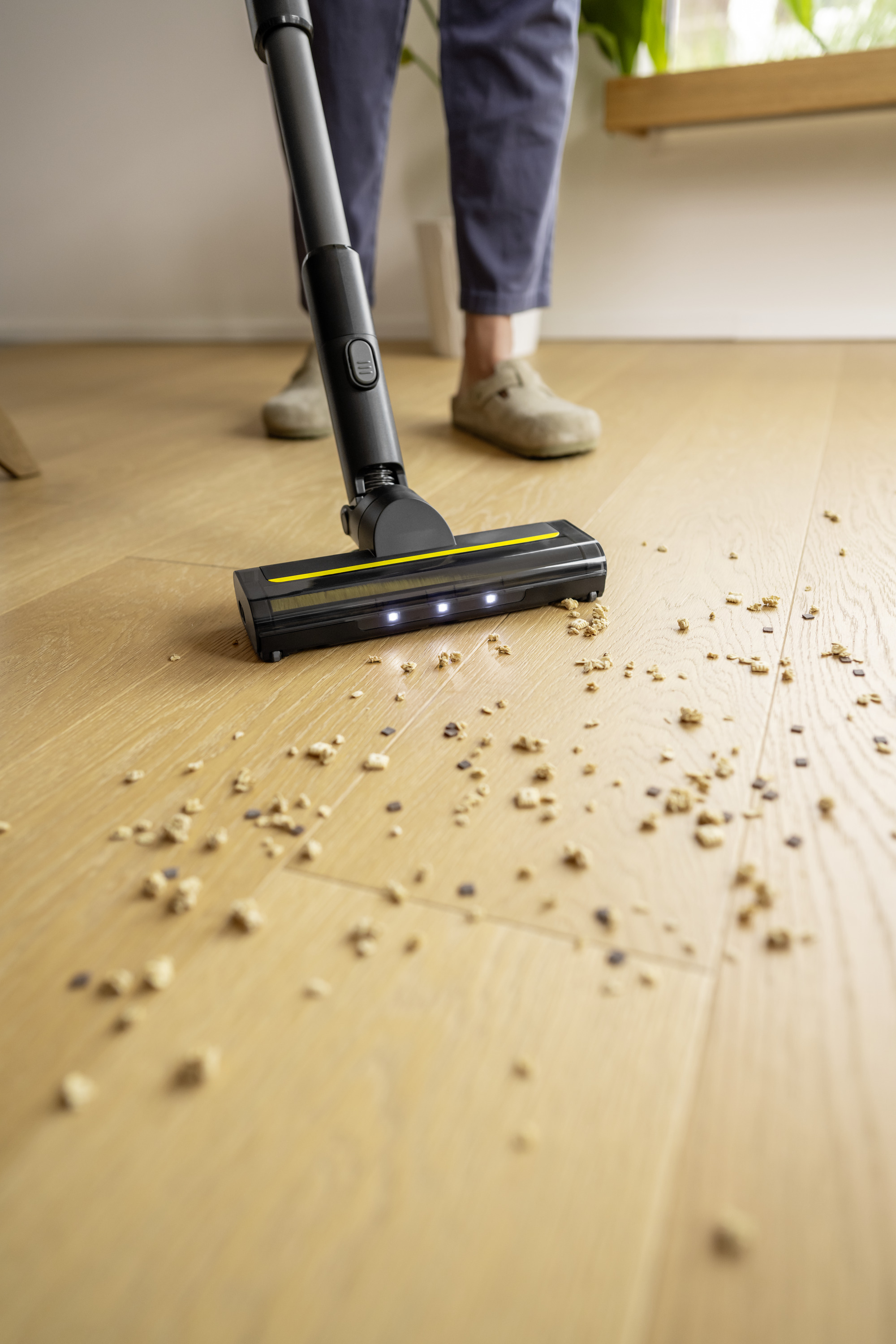 Ein Staubsaugerkopf mit gelbem Streifen saugt Krümel von einem Holzboden auf.