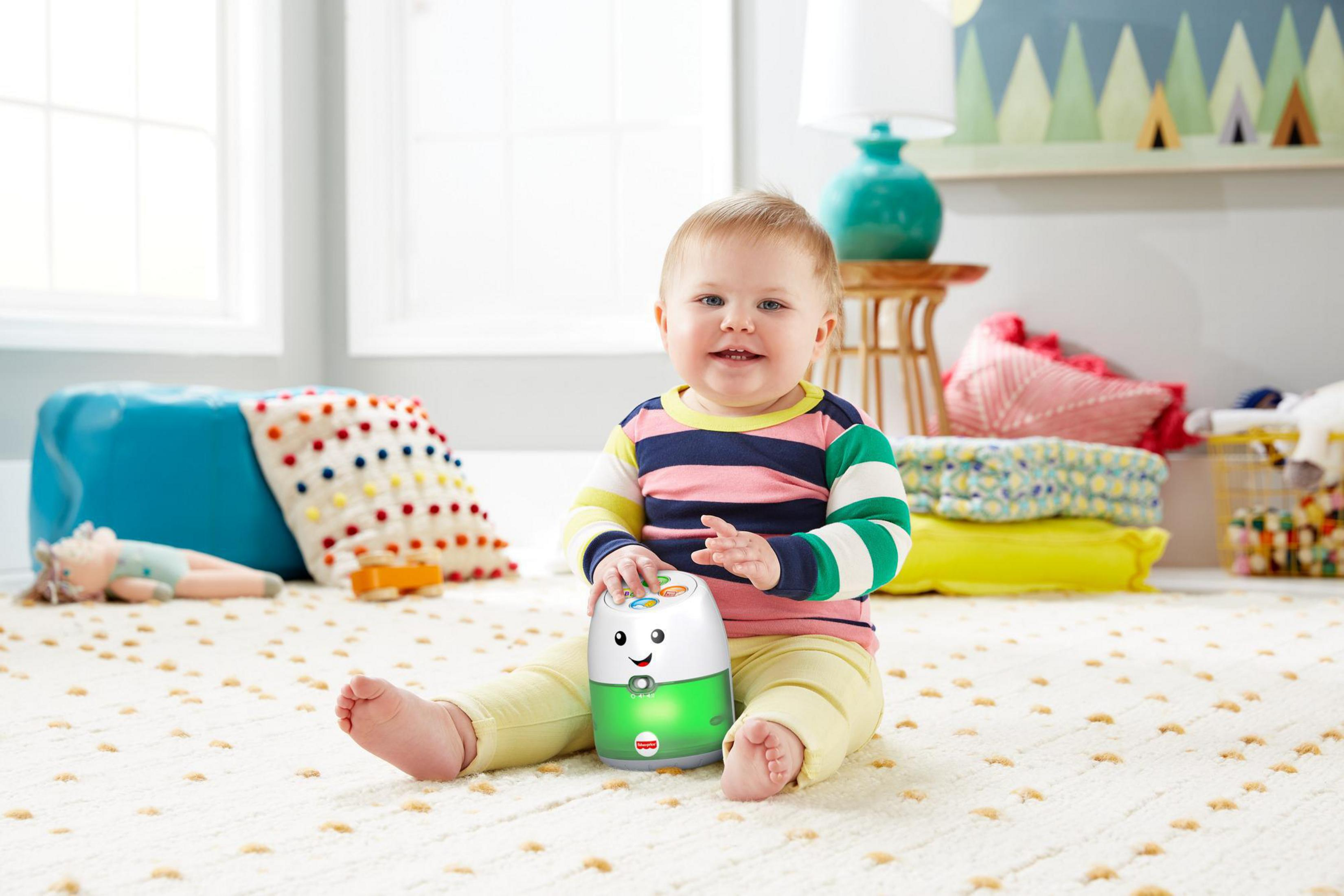 Ein Baby sitzt auf einem Teppich neben einem Spielzeug, das grün leuchtet.