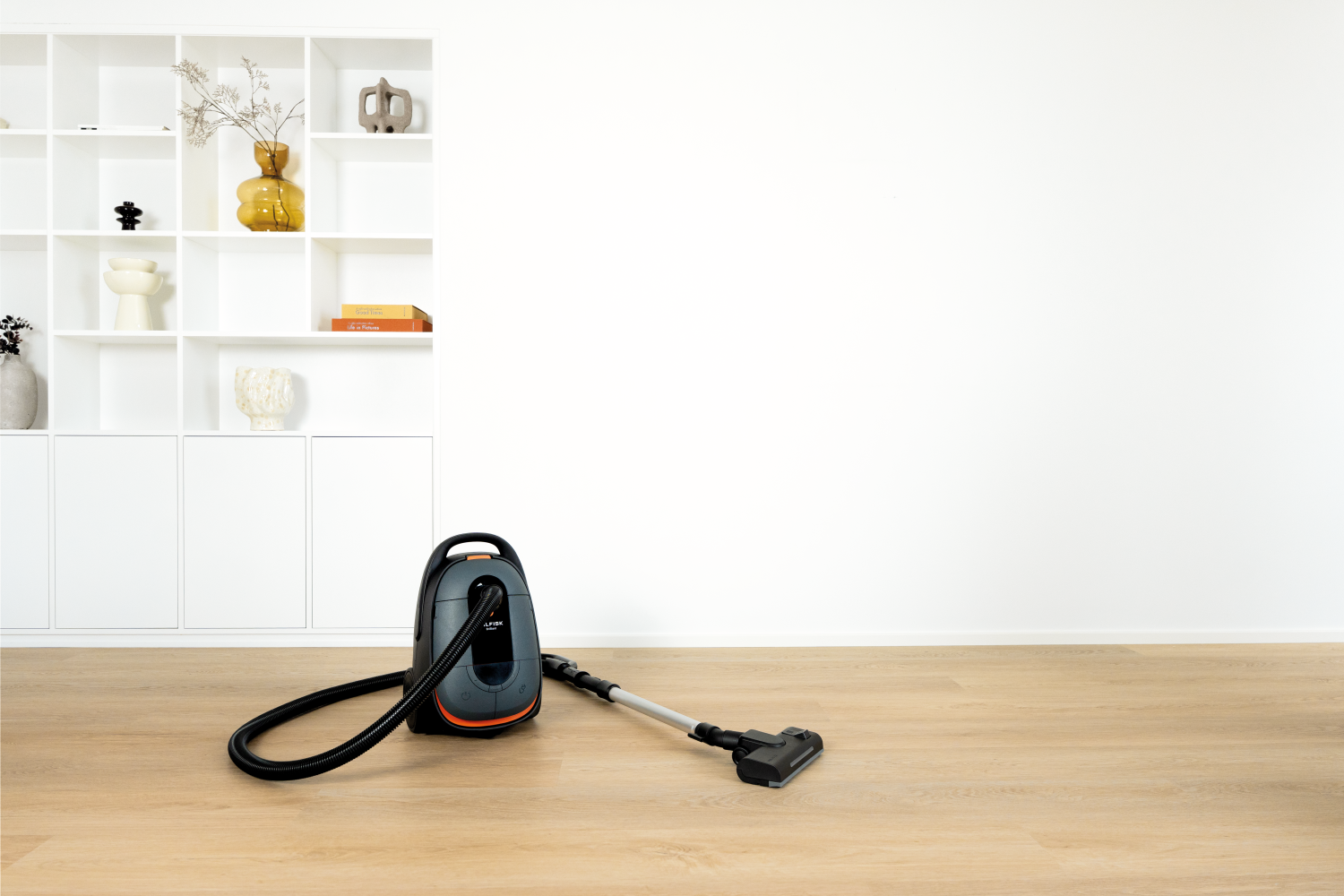 Ein grauer Staubsauger mit orangefarbenen Akzenten steht auf einem Holzboden.