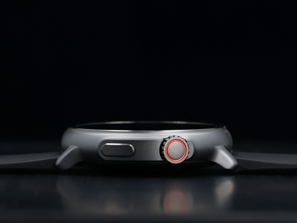 Szary smartwatch z czerwonym pierścieniem na koronie, czarne tło.