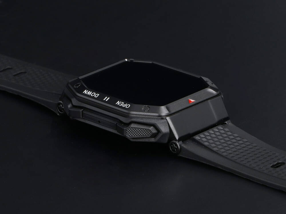 Czarny smartwatch z prostokątnym wyświetlaczem i gumowym paskiem na ciemnym tle.