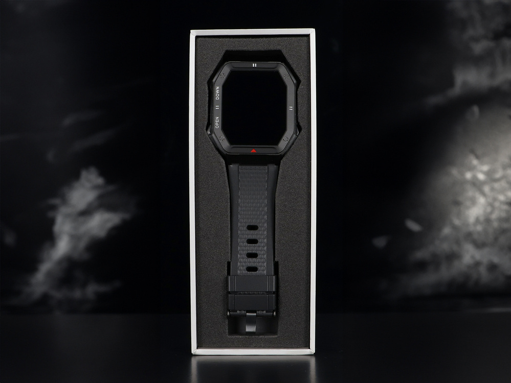 Czarny smartwatch z kwadratowym ekranem w białym pudełku, ciemne tło.
