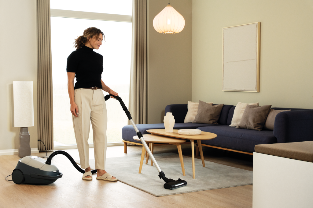 Mujer aspirando alfombra en sala con sofá, mesa de centro y lámpara.
