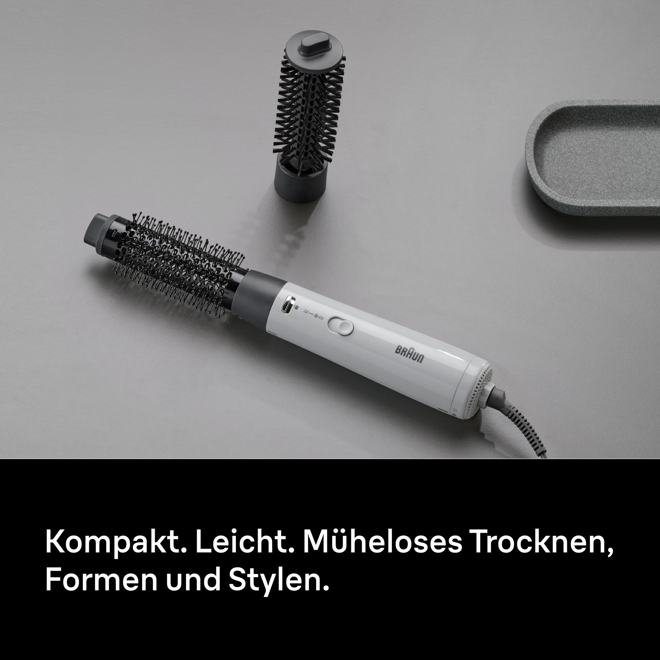 Ein weißer Braun Haartrockner mit aufsteckbarem Bürstenaufsatz liegt auf grauem Untergrund.