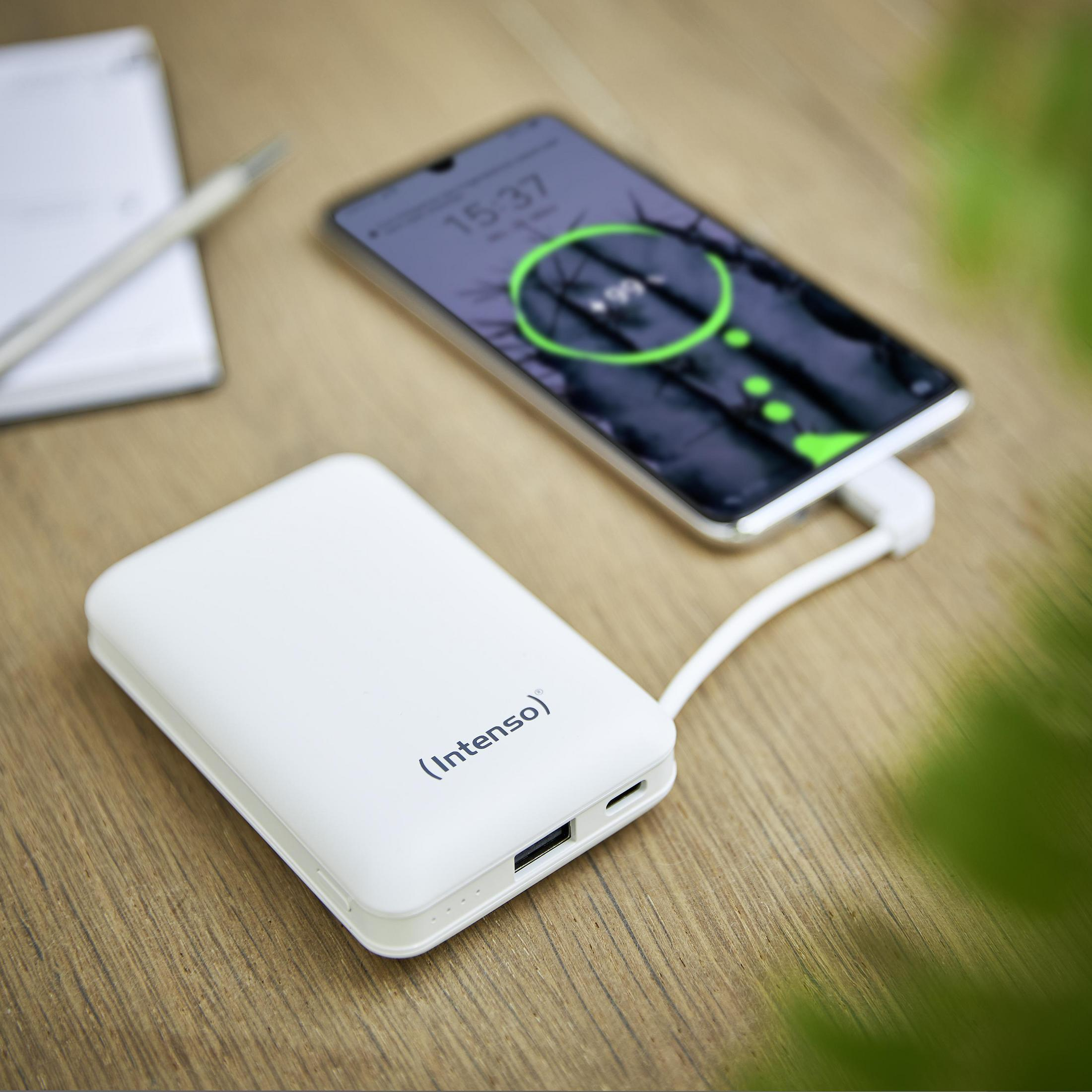 Ein weißes Powerbank lädt ein Smartphone auf einem Holztisch.
