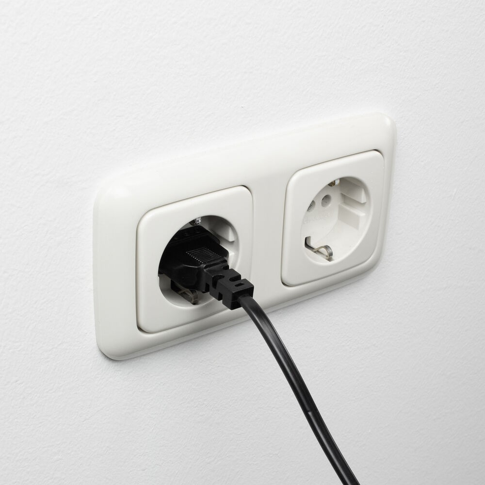 Ein schwarzer Stecker ist in eine weiße Steckdose gesteckt.