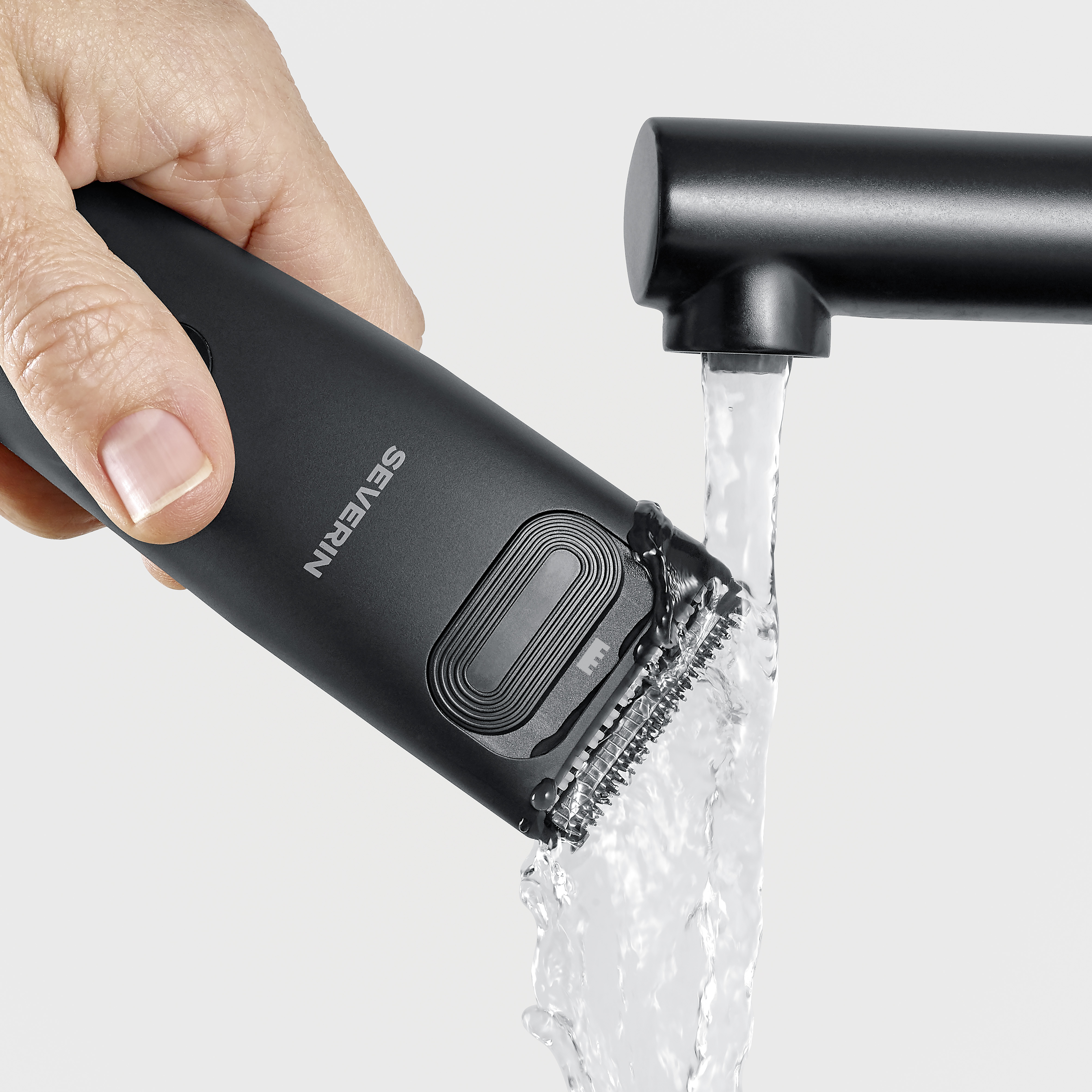 Una mano tiene un rifinitore nero sotto acqua corrente.